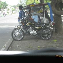 幹線道路脇でバスの降車客を自宅まで運ぶトライスクルタクシー