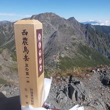 山頂から標柱越しに望む間ノ岳と北岳