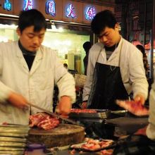 お店の外で羊肉の塊をスライスしてます