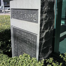 緑の植え込みの中に置かれた靴業発祥の地の碑の左側の側面です。