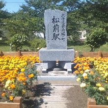 お花に囲まれた旧松前駅記念碑の様子