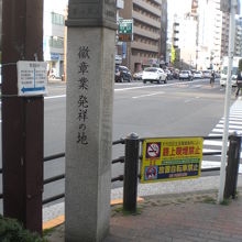 徽章業発祥の地の石碑と、背景の九段方向への目白通りの様子です