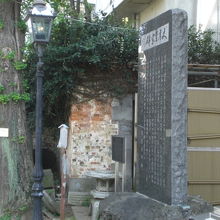 文具至宝碑の碑と解説板の横には、男坂のガス灯と老木が見えます