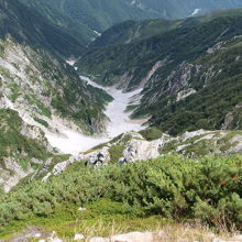 頂上から雪が残る谷を眺める