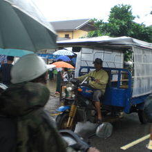 雨の多い中、ビニールの覆いをしつつ、乗客を探す小型バスです。