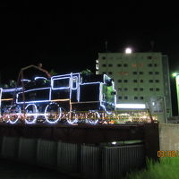 夜のホテル外観とライトアップされた駅前の機関車