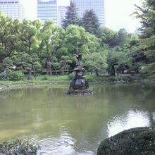 鶴の噴水のある雲形池です。濃い緑の樹々に囲まれています。