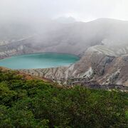 霧が一瞬晴れ、幻想的なエメラルドグリーンの火口湖が現れる。