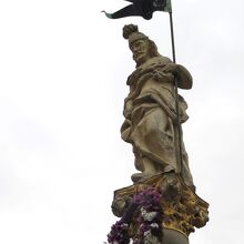 柱の上に立つ聖フロリアヌスの像部分。足元には捧げられた花輪が