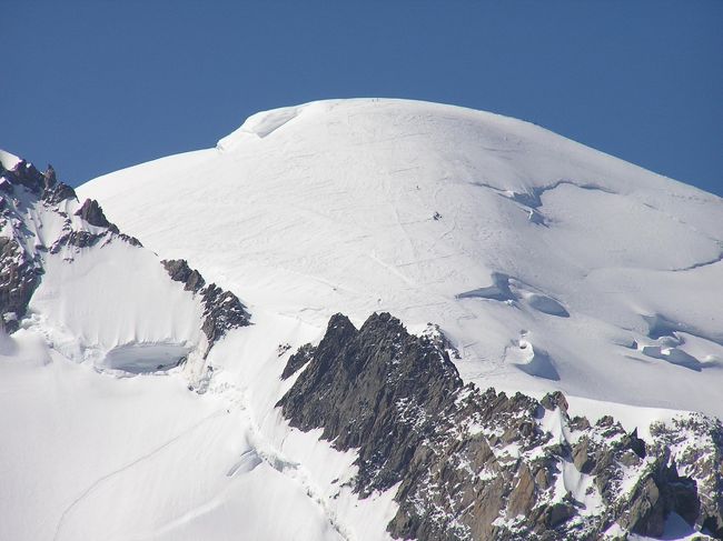 スイスアルプスハイキング旅行２００３の第５日目はシャモニーモン・ブランである。　スイスではないがアルプス三大名峰の旅としてフランスのヨーロッパアルプス最高峰であるモン・プラン連峰展望が予定に組まれている。<br />　<br />シャモニーモン・ブランについては１９９０年にヨーロッパ出張があってジュネーウ゜で２泊したときに日帰りで訪れたことがある。　<br />このときは天気はそんなに悪くは無かったがモン・ブラン連峰の頂上を見ることが出来なかった。<br />　<br />スイスアルプス三大名峰の旅では一般的に二つの名峰が見られれば良いということになっており、モン・ブラン連峰はヨーロッパ最高峰(標高：４８１０ｍ)であるために一番見れない確率が高いということを聞いていたので余り期待はしていなかったが、１３年ぶりで訪れるシャモニーモン・ブランは懐かしく、出来れば良い一日となってほしいと願った。<br /><br />　６月２２日の夕方午後５時半頃にスイス・フランスの国境を過ぎてから少し時間がたった後、レ・プラを少し過ぎ、シャモニーに近いところより針峰群が見えてきて、その奥のほうに真っ白なマシュマロみたいな山が見えたときには専用バスのツアー仲間はやや興奮して喜んでいた。｢モン・ブラン連峰が雲が一つも掛かっていないで見えるではないか」。今までの杞憂はなんだったんだろうかと思った。ツアー仲間全員は幸運を喜んだ。　<br /><br />今回のスイスアルプスハイキングツアーでは６月１８日〜６月２３日までは本当に良い天気が続くものだと思った。添乗員の方は｢皆さんは日ごろの心掛けが良いんですね。今迄、添乗員として何回もスイスアルプスハイキングに来ているけど、今回の天気が最高であると・・」と説明された。<br /><br /><br />＊写真はエギーユ・デュ・ミディよりモン・ブラン主峰をズームアップして撮影・・・写真を拡大すると登山者が見られる。