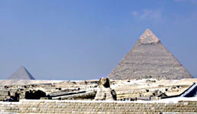 未だ多くの謎に包まれたピラミッド。実際に間近で見ると、本当にどうやってこんな大きな石を、こんなに高く整然と積み上げたのだろうと思う。ギザの三大ピラミッドの中でも、特にクフ王のそれは、大きさと美しさに圧倒される。そんなピラミッド、数年前の転落事故の後は登ることができなくなってしまったのだが、朝日コレクターの俺はどうしてもピラミッドの頂上から日の出を見たい。というわけで、同じ宿にいたチフス君（数日前まで腸チフスで入院していた）と一緒に夜中の登頂を試みた。<br /><br />夜更けになってカイロの宿を出てタクシーでギザまで行き、そこから住宅街を通ってピラミッドを目指す。途中、恐怖の野犬ゾーンをクリアし（噂では集団で遅いかかって来るとの事だったので、石とベルトを手に持って反撃体制を整え、かなりびびりながら身構えていたのだが、ただ近くに来て吠えるだけだった）、ピラミッド地区の塀まで辿り着いた。高さ3m程の石塀の上に、さらに3m程の金網が張ってある。<br /><br />しばらく塀に沿って歩くと少しだけ崩れている部分があり、そこから塀をよじ登る。さらに塀の上をしばらく歩くと、金網が裂かれている場所を見つけてそこから敷地内に忍びこむ。外側の5m程の土と砂の崖を登ると古墳群がある。ここからは物音を立てずに進む。ピラミッドの周辺は24時間体制で警備されているのだ。俺達は古墳を一つ一つ慎重に乗り越え、回り込み、クフ王のピラミッドに向かった。<br /><br />その夜は雲が月を隠していた。暗闇の中、うっすらとそびえる巨大なピラミッドは静かな迫力がある。古墳群を過ぎると、もうピラミッドは目の前だ。だが、警備の手薄な南東側に回り込むには、そこからさらにピラミッドの東側に面した遺跡群の後ろを通って行く必要がある。ピラミッドのすぐ周りでは、警官がパトロールしている姿も見える。緊張が高まる。<br /><br />遺跡群はそれぞれ大きさも間隔もバラバラに存在している。俺達は遺跡の後ろに身を隠し、ピラミッド側のパトロールの様子を窺おうとするが、こちら側からは何も見えない。息を殺し、遺跡の間に身をかがめてさっと走り抜ける。間隔が長い時には匍匐前進で進む。とにかく、見つかったら終わりだ。必死に息を殺しているのだが、まるで心臓の音が聞こえてしまうのではないかというほどにドキドキ鳴っている。<br /><br />ついに最後から二番目の遺跡まで辿り着いた。後一つで南東の角に回り込める。だがその時、前方の最後の遺跡の裏で何かがかすかに動いた！目を凝らすと、人影のように見える。まさかパトロールか？俺達は動きを止め、じっと息をひそめる。その影も動かない。長い沈黙。。。なんとなく、向こうも俺達の様子を伺っているようにも思える。それともただ人の形に似た岩なのか？<br /><br />すると突然、俺達が身を隠していた岩のすぐ近くから足音が！「やばいっ、逃げろっ！」そう言った時には既に遅かった。顔にライトを当てられ、その光の奥では銃がこちらに向けられているのが見えた。終わった・・・。俺達は両手を上げた。警官だった。前方の遺跡の裏の影が動き、もう一人の警官が現れた。そして俺達は詰所のような所へ連れて行かれた。<br /><br />詰所ではいろいろと質問されたが、全てアラビア語だったのでなんと言っているのかほとんど分からない。俺達はひたすらこっちの状況を正直に説明した。遺跡荒しなどと間違えられたら大変だ。「俺達はただピラミッドに登って朝日が見たかっただけだ」というのをジェスチャーで表現した。一見アホな光景だが、俺達は必死だった。<br /><br />その甲斐あってようやく理解してもらい、向こうの態度も和らいできた。和らいだと思ったら急にズル〜イ顔になってきた。それを待っていた。後は賄賂の折り合いさえつけば帰してもらえそうだ。警官達が要求してきたのは100ポンドずつだったが、帰りのタクシー代しか持ってないんですと言いながら、ポケットの中の有り金全部である10ポンド札を2枚出し、一人に10ポンドずつ渡してようやく解放された。<br /><br />だが俺達はそのまま帰らず、次の日の入場料と、カイロまでのタクシー代をけちって、そのままどこかに隠れて朝の開門時間を待とうという事になった。だいぶ冷えてきたので、俺達は古墳の一つに潜り込んだ。古代クフ王の親族の墓なのだろうか。「失礼します」と両手を合わせて挨拶をし、心地良い眠りについた。<br /><br />だがこれが、とんでもない祟りを呼び起こす事になろうとは・・・・。<br /><br />
