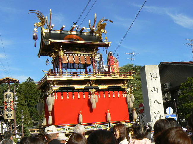 2006年10月9日（月）<br /><br />宮川の橋を渡れば、桜山八幡宮の大きな鳥居が、秋の日に金色に輝きながら、迎えてくれる。<br />しばらく先の正面に、森が見え、そこにお宮さんがある。<br /><br />鳥居からお宮さんに向かって、これまた金色に輝く祭り屋台が、ずらりと並んで見える。<br />一番手前は、「金鳳台（きんぽうたい）」だろう。<br /><br />台の上に立っている女性と、その右に座っているおじいさんが、目印である。<br /><br />左の女性はおたふくのようにふくよかな表情をしているが、案内書の説明書きには、武具をまとった神功皇后（じんぐうこうごう）となっている。<br /><br />左に座っているおじいさんは、皇后に仕えていた武内宿禰（たけのうちのすくね）で、抱いている赤ちゃんは後の応神（おうじん）天皇だろう。<br /><br />神功皇后は、実在したかしなかったかで二つの説があるようだが、日本書紀などによれば、妊娠したままで三韓征伐（西暦200年）に向かい、帰り道九州で出産、志免（しめ）でおしめを代えたと伝えられているようだ。<br /><br />明治の初めに紙幣にその像が使われたが、イタリア人のデザインを用いて、ヨーロッパ風の美人に描かれていたらしい。<br /><br />秋の空はいよいよ青く、金鳳台の屋根に輝く金色の鳳凰が、青空を背景に燦然と輝いている。<br />