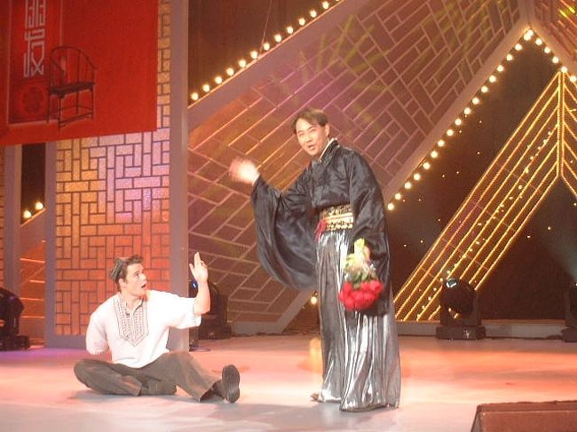 2002年『外国人中華才芸大賽』で総合部門銅賞を獲得したミュージカル寸劇「愛情故事」（中国でのテレビ出演（１）をご参照）は、その後、思わぬブレークをしました。<br /><br />中国各地の大学から「うちの留学生にもやらせたい」と北京テレビ局、珠海テレビ局、江蘇テレビ局に問い合わせが殺到。<br />南ドンが自身の留学先である南京へ戻ったあとも街角で「あっ、馬太郎（「愛情故事」の中での役名）だ！」と指差されることもあったほどでした。<br /><br />共演者のダニエルはもともと南京芸術学院の留学生で、中国での“外タレ”を目指して『外国人中華才芸大賽』でも賞取りを目指していました。<br />そして、銅賞ではありますが、見事に賞を取り、彼自身の活動範囲も広がったのです。<br /><br />「南ドン、オレと一緒に北京へ行こう！」<br />とダニエルから連絡があったのは『外国人中華才芸大賽』放送から2ヶ月以上も経った5月のことでした。<br />中央テレビ局の人気番組で『朋友』というのがあります。<br />角界の著名人物へのインタビュー番組です。<br />次回のゲストとして、外国人に中国文化芸能を指導し続けている年輩の演劇指導者が出演することになりました。<br />『外国人中華才芸大賽』での成功で、ダニエルはその先生の弟子になることができました。<br />そこで弟子として再度テレビで「愛情故事」を披露しなければならなくなったのです。<br /><br />中央テレビ局の番組収録ですから、もちろん北京へ行かなければなりません。<br />往復の飛行機代はもちろん中央テレビ局もちです。<br />『外国人中華才芸大賽』のときは珠海へ行くまで寝台列車に二日間も乗せられたので、これには大喜びしました。<br /><br />宿泊は中央テレビ局のホテル。<br />たった一日ですが「終日自由行動」の日もあって、「久々に北京の町が見れる」とダニエルに感謝しました。<br /><br />表紙の写真はテレビ収録中の演技の様子。<br />途中カットされることなく、一発でオーケーを得ました。<br />転んでいるのがダニエルです。<br /><br />そのダニエルも今や中央テレビ局専属の外国人タレント！<br />国際チャンネルにあわせると、しょっちゅう彼の顔を見ます。<br /><br />日本の外タレ同様、中国にはこんな外国人もいるのです。