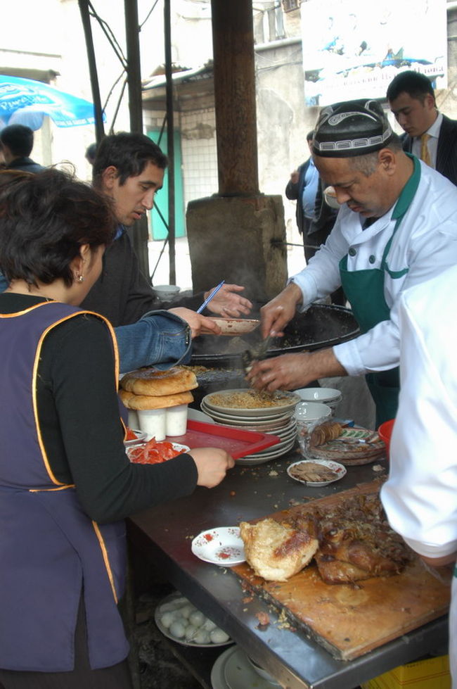 中央アジアのどの町でも食べられるプロフ、日本流で言えばピラフ、チャーハンは炒めるがプロフはお米から煮たご飯料理である。タシケントにはプロフセンターというプロフ専門のお店がワールドトレードセンターの近くにあり、ランチに食べに行った。<br /><br />このプロフセンター、ウズベキスタン料理屋が並ぶ一角にありメニューはプロフだけの専門店。作り方は大きな鍋に肉(ビーフorラム)の塊、お米、香辛料などを大きな鍋にいれ炊き込む。これがたいへん美味。<br /><br />通訳と一緒に行ったのだが、プロフとっしょにリピョーシュカ(釜で焼くパン)、サラダを注文した。大きな皿に盛るばあいと個別に盛る場合があるようだ。プロフの上には一緒に煮込んだ肉の切り身(ビーフ)がのっている。ご飯とパンを一緒に食べるところがウズベキスタンらしい。それからグリーンティーを注文した。席は2階の全体がよく見えるテラス席、ウエイトレスや客の動きがよくみえた。テキパキとシステマチックに動くさまは感嘆に値する。隣近所の事務所からプロフだけを買いに来る客もいる。また、ウズベキスタン人だけではなくロシア系の客も目に付いた。<br /><br />遅いランチ時間に行ったがまだまだお客でいっぱい、5釜あるプロフはその日の終盤、残り少なかったがなんとかプロフにありつくことができた。<br /><br />プロフについて<br />http://www.orexca.com/cuisine_plov.shtml