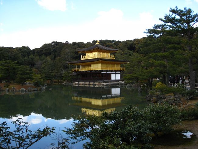 冬の金閣寺に行ってきました。○【金閣寺】(歴史) この地は、鎌倉時代に西園寺公経(さいおんじ きんつね)の別荘・北山第(きたやまだい)があったところ。それを応永4年(1397年)に3代将軍・義満が西園寺家から譲り受け、山荘・北山殿を築いて住んだのがはじまり。贅を凝らした金閣を中心とする建物や庭園は、極楽浄土をこの世に表したものとされる。金閣は公家の伝統と武家の先進性、さらに唐様をも取り入れて融合した新しい文化ー北山文化の象徴となったのである。同15年(1408年)、義満の急死後は、その遺言により夢窓国師(むそうこくし)を開祖として禅寺に改め、義満の法名から鹿苑寺とした。(観賞ポイント) なんといっても金色に輝く3層の楼閣・金閣をはずすわけにはいかない。実はこの建物は釈迦の骨を祀った舎利殿である。1層の法水院(ほっすいいん)は寝殿造り、2層は武家造りで潮音洞(ちょうおんどう)と呼ばれる。そして最上階(3層)の究竟頂(くっきょうちょう)は禅宗仏殿造りと、三つの様式を見事に調和させた室町時代の代表的な建築だ。さらに、2層と3層は漆の上から純金の箔が張られ、屋根はさわらの薄い板を何枚も重ねた杮葺き(こけらぶき)の宝形(ほうぎょう)造り、屋根の上には中国でめでたい鳥とされる鳳凰が輝いている。 このあでやかな金閣をより美しく、神秘的に見せるのが鏡湖池(きょうこち)だ。水面には大小の島々が浮かび、ほとりには数々の名石が配されて、西方にそびえる衣笠山を借景とした池泉回遊式庭園となっている。石は創建当時、諸大名が競って献納したというもので、それぞれに大名の名がつけられている。そして、池の水面に映し出される黄金に輝く金閣・・・・・。いわば自然の「鏡」。金閣寺の美は鏡湖池とセットでこそといえるだろう。