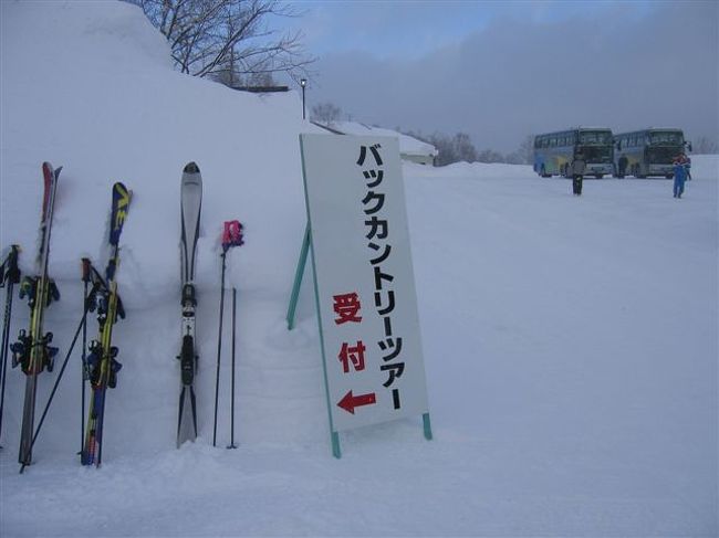 ２月１６日(土曜日)、志賀高原のバックカントリーツアーに行ってきた。バックカントリーとは、辺境とか奥地とか、田舎などの意味があるが、スキーでは、ゲレンデを離れ、雪原を大自然を楽しみながらツアーすることで、このところ、じわじわと人気が高まっている。今回は、志賀高原から草津への距離にして１３キロのツアーに参加した。スキーシーズンになると定番となった「私をスキーに連れてって！」（ワタスキ）の影響もあって、一度は体験しようと思っていたツアーで、志賀高原観光協会が主催している。ツアーの申し込み開始から３日で半数の日が満員となる盛況ぶりで、特に申し込み初日は平日の午後１時からの受付というのに、申し込み殺到でコンピュータがトラブルを起こしたほど。募集は観光協会のホームページでの告知だけというのにこの騒動。ワタスキの知名度もあってか、このツアーの人気ぶりがよくわかる。<br />　われわれ３人は、ツアー初日のコースにエントリー、予約殺到の中、無事受付が終了してからは、連日の打ち合わせ。子供の頃の遠足の気分にも似た高揚感をこの年になって再び体験するとは思わなかった。<br />　ツアーが近づいてくると、持参する食料やランチタイムの楽しみ方などの相談にも熱がこもる。一方で、天気図をにらみ、この週に入って勢力を増した冬型の低気圧の行方がなんとも気になる。予報はどんどん悪くなり、もし中止になったらという想定も現実味を帯びてきた。<br />　前日は、常宿の熊の湯ホテルに夜１１時過ぎに到着。早速温泉につかり、雪の降りしきる中、露天風呂で空を見上げながら、ツアーへの期待を話しあう。しかし、衰えない雪の勢いに、半ばあきらめの心境だった。救いは、中止の場合、前日の夜９時までに連絡があるということで、この連絡がなかったこと。１６日の朝、７時までに連絡がなければ決行だ。<br />　温泉からあがって、ビール片手にワタスキを鑑賞。早く寝るべきと思いながらついつい全部見てしまう。ツアーへの期待感はいやがうえにも増すが、この時点でも降り続く雪の勢いに中止を覚悟した。<br />　それでも朝６時に睡眠時間３時間あまりで起床。外を見ると雪がやんでいる。青空もところどころにのぞき、これなら決行と、荷物の最終チェックをして、ウエアに着替え７時前には準備完了。昼食用にカップヌードルと燗番娘（日本酒）を確保して、仲間は食堂に熱いお湯をもらいに行く。いつもに比べ、なんという手際のよさ。受付は８時半、宿から受付会場までは車で１５分ほどなので、８時過ぎに出ればいいのに、なんとも落ち着かない。午前７時を過ぎても中止の連絡がない。ようやくツアーが現実のものとなる。朝食は７時半から、少し早くあけてもらって、それでも、ものの２０分で終了。受付会場には８時１５分前には到着してしまった。受付開始時間にはいたるところからスキーを担いで続々集合、ほとんどが定時で受付を終えた。参加の記念に目印となるバンダナが配られる。このあたりは志賀高原らしい、センスの良さで感心した。<br />それにしても顔ぶれを見ると、自分も含め若者がほとんどいない。ワタスキ世代といえばそういうことだが、どう見ても平均年齢は４０歳以上、中には７０代後半の方もいる。若者はどこに行ってしまったのだろう。<br />　オリンピック記念の98会館前を出発したのが午前9時、バスは熊の湯に向かう、ちょうど1時間半前に出発した熊の湯ホテル前に戻ってきた。バスはこのあと草津へ向かい、われわれを迎えてくれる。<br />　熊の湯スキー場のリフトで山頂に上がり、ツアーコースで横手山に。さらにリフトを乗り継いで横手山の山頂に到着。そこで記念写真。参加者５８名ともなるとさすがに大勢だ。コースの案内人となった協会のインストラクターをはじめリーダーも入れると７０人に及ぶ。記念撮影のあと渋峠を滑り降り、渋峠ロッジ前で昼食のパンが配られる。 <br />　  <br />最終のチェックとトイレ休憩を取って、いざ出発。渋峠のリフト乗り場から志賀草津道路の北側へ１５０メートルほどのところからコースに入る。<br />前夜の雪が降り積もり、先頭はまさにラッセル状態。コースはところどころの木に目印となる黄色い布がつけてある。きちんとした看板ではなく、リーダーが案内してくれなければ見落としがちで、このコースは、単独行動はできないことを痛感。ラッセルをしながらリーダーが進むところを６０人のグループがついていくが、深い雪が行く手を阻んで、大渋滞。少しずつ、ほとんどボーゲンで進む。途中くぼみのようなところもあり、転倒する人も多いが、少しでもコースを外れると新設の中に突っ込んで容易には起き上がれない。立ち上がれないからとスキーを外そうものなら、もっと深みにはまってしまう。ゲレンデスキーとは違う緊張感も漂う中で、慎重に少しずつ進んでいく。コース自体はほとんど下り。３月になって、雪が落ち着けば滑っていけるというところだけに、いかにスピードを制御するかが課題で、一本道の中で、少し油断すると制御不能になり、人の密度が高い中、よけきれずに、自分も２度ほど頭から１回転した。<br />　１時間ほど進むとこのツアー最大の斜度のある斜面に出る。ツリーランを楽しむには最高のコンディションで、ガイド役のリーダーからも「前の人が行ったところばかりでなく、新設を思う存分楽しんでください」と声がかかる。しかし一歩、新雪に踏み入れれば、雪は膝上にくる。地形もわからない中で、木と木の間をスキー操作するのは至難の業。急斜面の新雪でのツリーランの難しさを痛感した。ワタスキの世界は奥が深い。<br />  <br />　急斜面を何とか降りると、景色が開ける。芳ケ平ヒュッテの赤い屋根が見えてくる。ここから少し登りの斜面が続く。滑り降りるよりも一定のリズムで進める。日ごろゲレンデでは一歩でも上りを少なくしようとするが、ここでは、上るのも苦にならないのが不思議だ。程なくして芳ケ平に到着。通年人が住んでいるという芳ケ平ヒュッテでトイレ休憩。辺境の地にどうやって住んでいるのかという興味がわく。<br />　さすがに体力を使って、空腹になってきたころ、一本杉という雪の中の広場に到着。ここで昼食となった。雪の上に自らのスキーを裏返しておいて、その上に座るが、ここも新雪が当然ながら積もっていて、動きが取れない。何せ足を踏み出せば、埋まってしまう。やっとの思いでスペースを確保して座ったところで、スタッフの方からワインをいただく。自然の中でよく冷えた赤ワインは本当にうまかった。なんとも行き届いたツアーだ。自らも、この時間のためにわざわざ運んできたスパークリングワインをおもむろに取り出し、栓を抜く。雪原の中でのスパークリングワインは本当にうまい。パンとカップヌードルとスパークリングワインという奇妙な取り合わせだが、こういう環境では実にうまいのだ。他の参加者もバーナーでお湯を沸かしてコーヒーをつくったり、ビールで乾杯したり、思い思いにランチタイムを楽しんでいる。この時間もバックカントリーツアーの欠かせないひと時なのだと思う。仲間３人でスパークリングワイン１本は、ちょっと多かったようで、少し酔っ払う。もう少し休憩していたかったが、ラッセルしながら進んで、いつもより時間がかかったらしく、あわただしい出発だ。あと残りはどのくらいかわからないが、酔っ払いにはきつい。残りはどのくらいかわからないが、大丈夫か。<br />再スタート後は、しばらく上りが続き、下り始めたところで常布の滝という凍った滝に出る。７０代後半と思しき男性が、もう来れないかもしれないから写真に撮っておかなくてはといわれたのが耳に残る。その後ダムの前を滑り降りたあと、また、集団ができていた。一人ずつゆっくり進んでいく。噂の一本橋だ。少し上り勾配だが、ストックをつくところがないほど狭い。酒の回った身には少々恐怖感もある。それが３箇所もある。なんとか橋を無事渡り終えたら、後は上り、しばらく上ると草津スキー場の駐車場が見えた。国道のガードレールの脇を滑り降りて、途中で道路を渡るとそこは草津スキー場だった。到着だ。１３キロでこんなに景色が変わるのかというほど、熊の湯や渋峠のスキー場と雰囲気が違う。マンション群にリフト待ちの列、東京圏のスキー場という印象で、スキーを履いて移動してきたとは思えないほど空気が違う。草津国際スキー場はほんの３０秒も滑ったところで全員集合。なんともいえない満足感があった。<br />このあと草津温泉で一休み。熊の湯ホテルで温泉三昧のあとだけに感激は少なく、むしろ健康ランドのような湯に物足りなさを感じた。あとは、バスで帰るだけ。バスの中では志賀高原ビールも配られた。本当に至れり尽くせり、ガイドの団長の石川さんが志賀高原や草津界隈の由来などを解説してくれる。本当に山が好きなんだろうなあと思う。バスは３時間かけて志賀高原に戻り、午後６時過ぎに解散となった。疲れたが貴重な体験。来年は草津ではなく万座か。やばい、癖になりそうだ。<br /><br />