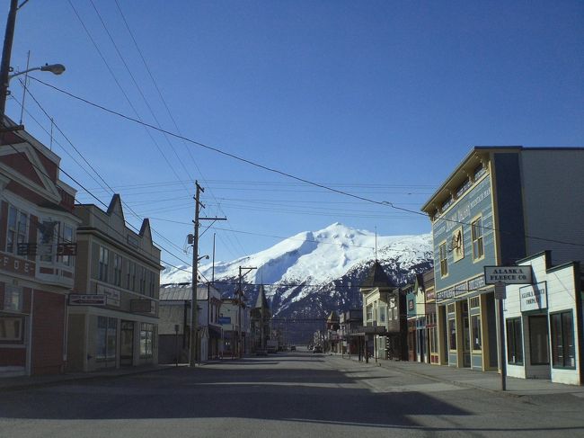 アラスカ州スキャグウェイの紹介です。<br /><br />スキャグウェイはアラスカの州都ジュノーから、北西約145kmに位置する、タイヤ江に面した人口約800人の小さな街です。<br />夏場（5月〜9月末のクルーズ船が停泊する期間）は、多くの観光客で賑わいます。<br /><br />スキャグウェイで著名な人物の一人として、蒸気船の船長でビジネスマンだったウィリアム”ビリー”ムーアがいます。<br />彼はゴールドラッシュ前の1887年、カナダ・ユーコン地方のクロンダイクにゴールドが眠っていると信じ、息子と共にスキャグウェイ河口に家を構え、”ムーア波止場”（現在多くの大型クルーズ船が停泊する波止場です。）を建設しました。そこからのルートが最もゴールドに近いと信じたからです。<br /><br />またランドルフ”ソフィー”スミスも有名です。<br />彼は裕福な家に生まれ、弁護士の父親を持ちながら、自分自身はギャングとなった人物です。<br />彼はスキャグウェイであらゆる詐欺・ギャング行為をし、1898年7月8日にフランク・レイドとの決闘で銃弾を胸に受け、亡くなりました。<br /><br />フランク・レイドはこの時の決闘で受けた傷が致命傷となり、12日後に亡くなりました。<br /><br />マーティン・イジェンは、ゴールドラッシュ時にスキャグウェイにやってきた探鉱者でしたが、ホワイトパス・ユーコン鉄道の建設を支持したり、現在も「ストリートカー」として知られているツアーを始めたり、ソフィー・スミス博物館を開いた人物です。彼によって1900年代初期のスキャグウェイの歴史は守られたと言われています。