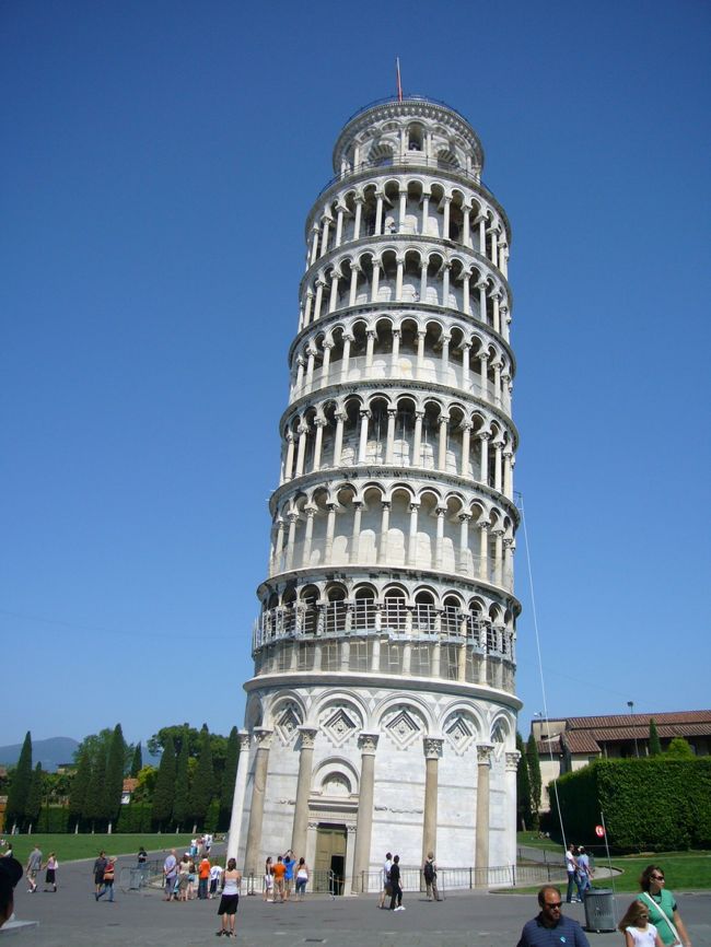 建築が傾いてしまったために、世界的に　ものすごく有名になった建物といえば、もちろん　ピサの斜塔（Torre di Pisa）ドゥオーモの鐘塔として　1173年に建て始めたんだけど、地盤が　弱かったので　南に傾いてしまったのだ。<br /><br />ピサの斜塔が傾いているのは世界の常識。でも、百聞は一見に如かず、ということで　実際に　どれぐらい　傾いているのか　見に行ってきた。<br /><br />ツアーエスコートとして他の観光客と一緒にバスに乗りこむ。<br />ピサの斜塔が建っているドゥオーモ広場（Piazza del Duomo）は　バスでは近づけないので　少しはなれたところでおろされる。おそらく違法であろうと思われる　路上販売のおじさんたちを横目に　広場を目指して　さっさと歩いていく。すぐそこに　見えている斜塔なんだけど、思ったより距離がある。ようやく　人ごみを抜けて　ドゥオーモ広場が目の前に広がる。<br /><br />ピサの斜塔を全体像を見て、最初に思ったのは「思ったよりも　傾いている！！！」<br />傾斜を防ぐために　修復作業が続けられているんだけど、それでも　毎年　少しずつ傾き続けているんだとか。前に写真で　見たときより、実際　もう少し傾いた、ということなんだろう。<br /><br />遠近法の利用で　ピサの斜塔を支えるようにして　写真を撮っている人がたくさんいた。<br /><br />斜塔のふもとまで　来てみると　地盤沈下している様子がよく分かる。ワイヤー（？）みたいなもので　補強してあるのが　なんともリアル。ちゃんと　そのすぐそばには　どういうことが原因で　こんなに傾いてしまったか、などが　詳しく説明された看板がたっていた。<br /><br />ところで、世界遺産にも登録されている　このドゥオモ広場には　ピサの斜塔（鐘楼）だけじゃなく、洗礼堂、大聖堂（ドゥオーモ）、墓所回廊も建っている。（実は来るまで　知らなかった・・・）どの建物も　すごく立派で印象的だ。それから　付属美術館では　ドゥオーモの中にあった彫刻なんかが　展示されている。<br /><br />お土産物やさんが　たくさん　並んでいるのが　観光地らしい。<br /><br />広場を満喫したところで　バスに戻る途中、路上に店を広げているおじさん、お兄さんたちが　機敏な動きで　荷物をまとめはじめた。なにかと思えば、おまわりさんが　見回りに来たようだ。コピー物を売っているのは　もちろん、ここで　お店を開くのは　違法なんだろう。ただ、現行犯じゃないと　逮捕できないのか、明らかに商売をしている人たちを　捕まえることなく、おまわりさんは　ただ　歩いているだけだ。<br /><br />斜塔にも感動したけど、このおじさんたちの手際のよさにも　感心してしまった。