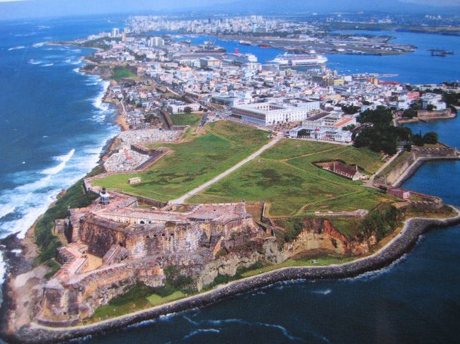 日付が変わってクリスマス。今回のクルーズのメインの寄港地、米領プエルトリコ(Puerto Rico)のサンファン(San Juan)へ。以前から一度来てみたいと思っていた場所だけど、クリスマス休日なのが残念。海賊に備えるためのエル・モロ要塞を観るには、やはり海側から。早朝から甲板で入港していく様子を眺める。サンファンはプエルトリコ島の北側に突き出た岬に創られた街。天然の良港なのがよくわかる。これじゃぁ米国に狙われるのも当たり前。スペインも気の毒だったけど、住民にとってはアメリカ人になれてよかったのかな。左側に見える世界遺産の旧市街と右側に見えるビル街の新市街のコントラスト。やっぱり米国の一部だと感じる。<br />0800入港後に上陸。スペイン植民地の香りがするカラフルな旧市街を抜けて、突端のエル・モロ要塞を目指す。岬の北側の外洋に面したところの波の高さを見て、穏やかな湾の内側との違いに驚く。<br />エル・モロ要塞に着く直前、スコールに遭うのも南国気分。要塞に教会・墓地がつながっているのが面白い。やっぱり休みで中には入れず。旧市街で開いているレストランを見つけ、モヒートと地元料理で疲れを癒す。キューバ旅行以来のモヒートのミントの豊富さにカリブ海を実感。<br />1700出港。あとはクリスマスのフォーマル・ディナーとショーを楽しむだけ。たまには夏のクリスマスもいいかな。