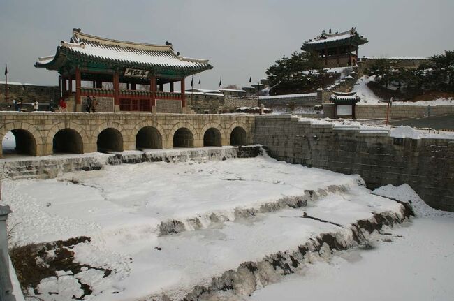 2010年1月10日、世界遺産、水原・華城(スウォンファソン)へ行く。<br /><br />年の瀬からソウル一帯は1937年以来という寒波と大雪に見舞われ、水原も白一色の世界。ソウル発8:25のセマウルで水原まで行き、駅前からバスに乗ってスタート地点の八達門で下車、そこから時計回りに城郭を一周するが、午後からは気温もいくらか上がり、さほど寒さを感じることなく完歩することが出来た。<br /><br />表紙の写真は「華虹門」(ファホンムン)。この楼閣は水原川にかかる水門の上に立てられている。ご覧のとおり川は寒波のため凍り付いているが、水は氷の下を流れている。右側にあるのは「訪花随楊亭」(パンファスリュジョン)といい華城を造った正祖が酒宴を楽しんだといわれる建物。<br />