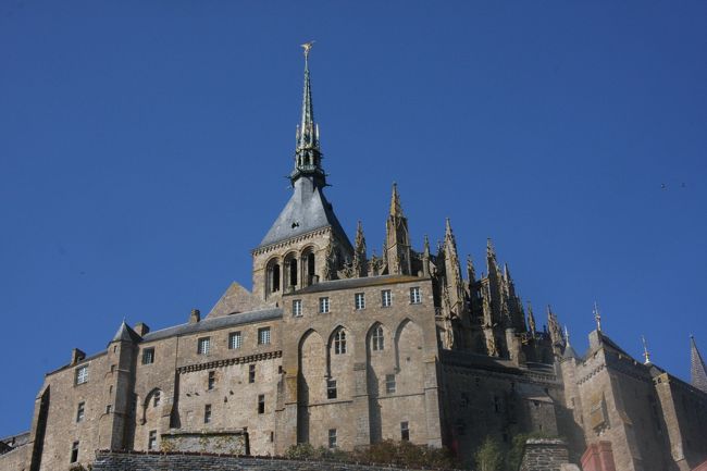 モン・サン・ミッシェルの修道院とミカエル像　2008.10.11 14:40<br />Mont St. Michel and Stature of St. Michel<br />────────────────────────<br />&lt;2011.3.11東北関東大震災に際して&gt;<br />この度の地震・津波で被害に遭われた被災者の皆様には心よりお見舞い申し上げます。<br />またこの場を借りて東北関東大震災の犠牲者の霊に心より哀悼の意をささげます。&lt;献歌&gt;<br />みぞうなる　じしんつなみが　たみおそう　やまとのくにの　かみはいずこに<br />（未曾有なる地震津波が民襲う　大和の国の神は何処に）<br />────────────────────────<br />2010年6月8日に公開した本編が、おかげさまで予想どうり好評でしたので、掲載できなかった多数の写真を編集して続編を作りました。<br />写真は表紙を含めて78枚で本編を合わせると118枚です。<br />続編ではカーンを出発してモン・サン・ミッシェルに約22時間滞在し、ブルターニュ地方の中心都市レンヌの駅までの行程をスライドショウのようにご案内します。<br />写真の説明は要所を除き簡単にしました。旅行記には本編（永久保存版）http://4travel.jp/traveler/810766/album/10468332/<br />と重複箇所が多々ありますことをお断りしておきます。<br />また写真も続編の20枚を本編に繰り入れたためその分が重複しています。<br />　　　　────────────────────────<br />2008年10月11日（土）<br />前日泊まったオンフルールからのタクシーは8時少し過ぎには日の出前のカーンに着いた。<br />駅の売店で朝食のサンドイッチとコーヒーを買って列車を待った。<br />8：43発の３両編成のブルーの列車はカーンCaenからコタンタン半島（コタンタン半島の先端には1964年、カトリーヌ・ドヌーブ主演のフランス映画「シェルブールの雨傘」の舞台シェルブールの街がある）を西へ進み、主要な駅BAYEUX,SAINT-LOを通り,COUTANCEから南下してPONTORSON MONT-SAINT-MICHEL（モンサンミッシェル）まではちょうど２時間で着いた。車窓の景色は牧草地、とうもろこし畑、大きくない森などで山は見えない。<br />線路の両側にはずーっと木が植えてあるので景色を写すのは難しい。マニュアルフォーカスにして距離を∞にセットしておいて、植え込みの切れ目の瞬間にシャッターを押すしかないがそれなりにスピード感が出て悪くはない。<br /><br />モンサンミッシェル駅は人気の高い観光地の最寄駅とは思えないひっそりとした小さな駅で、世界遺産登録で人気化する以前と変わらないのだろうと想像した。<br />駅前に止まっていたバスがモンサンミッシェル行きで、運転士に聞くと11：22発で10分少々で着くといっていた。予約したホテルは終点より手前１Km（実際は２Km）のホテル地区にあると教えてくれた。<br />Saint Aubert Hotelのチェックインは３時からなのでキャリーケースを併設のレストランに預けてモンサンミッシェルへ向かった。<br />ホテル地区を抜けると頂上に修道院を擁する特徴ある島が見えてくる。<br />まず目に入ったのは手前の草原でもくもくと草を食べている羊の群れで、首から上と脚が黒いサフォーク種である。まっ昼間に着いたのでやや単調な景色だが、夕方が楽しみだ。<br /><br />島に着いて狭い上り坂の両側にひしめくように並んだレストランや土産物屋の一画を過ぎて何カ所かの長い石段を登ると修道院の入り口がある。<br />天気が良すぎてコートを脱いでも暑いほどである。修道院の見学のためにしばらく並んだが、列が一向に進まないので入場はあきらめた。キリスト教徒でもないし、まあいいか。43年前の1965年に来た時、少ない時間に急いで息を切らして上まで登った記憶がある。<br /><br />修道院の尖塔は島内に入ってしまうと見える場所が限られてしまうが、周囲の海は干潮で遠くまで干潟になっており、ウォーキングツアーの人々までがよく見える。<br />降りてくる途中で周囲の町並みの屋根や煙突、屋根裏部屋など、下からは見えないものが見られて面白かった。どこを歩いても階段と坂の連続で、現代のバリアフリーの概念の対極をなすもので歴史の重さを感じさせる。<br /><br />帰り道でも羊の群れを見に行くと、自分の影と一心同体になって黙々と草を食んでいた。<br />ホテルに戻ってチェックインを済ませ、昼の部を締めくくる入浴・昼寝タイム。<br />三つ星だがバスタブがあるのがありがたい。<br />７時ごろ三脚とカメラだけを持って夜景の撮影に出かけた。ちょうど沈む太陽の撮影にギリギリ間に合った。日没後の空の色の変化はいつ体験してもその美しさに感動させられる。<br />赤から赤紫、やがて赤みが薄れてトキ色、さらに赤みが消えて青灰色、薄闇の青、群青の濃闇へと一時間もかからない。やがて少しずつライトアップが始まった。<br /><br />西の空の残照とライトとの割合の変化で微妙に変わってゆく夕景色を撮っていると、今自分がそこにいて、何の制約もなくそれが出来ることに感謝し、そのこと以外何も考えていない。<br />帰りがけにホテルの隣のレストランLe Bergerieで夕食をとった。前菜のスモークサーモンとメインには羊のロースト（超美味）、赤ワイン、紅茶（E35）。心の中で羊に手を合わせる。羊さん　ありがとう。<br /><br />10月１２日（日）<br />モンサンミッシェルの夜明けを見ようと出かけた。８時過ぎても地平線あたりの雲が邪魔して太陽がなかなか顔を出さない。<br />日の出前の空を海から陸に向かって多数のカモメと思しき群れが、時にはばらばらに、次には隊列いわゆる雁行をなして飛んで行くのがその鳴き声と共に印象的であった。<br />これこそ私の旅の目的である、非日常の体験である。<br /><br />８時４０分ごろになってやっと雲間から太陽がのぞいた。おもわず両手を挙げて拝んだ。修道院のガラスに反射する朝日を眺めて写しモンサンミッシェルの予定を完了。<br />今日の目的地ブルターニュ半島西端のカンペールにはレンヌまでバスで行き、そこから列車に乗る。レンヌ行きのバスは9：30発でレンヌには10：50に着くはずだったが、レンヌ市内で日曜日の市民マラソンに出くわして通行止めに会い、しばらく待ったが通れそうもないのでいったん市外に出てから駅の反対口に着いた。<br />　　───────────────────────────<br />大量の写真をご覧いただき、お疲れ様でした。<br />モン・サン・ミッシェルを旅行した気分になっていただけたでしょうか。<br />今回紹介したモン・サン・ミッシェルの前後の「ノルマンディー・ブルターニュの旅2008」は7月から順次公開しました。主な旅先は、印象派の画家クロード・モネの活躍した地域を訪ねたので、ルーアン、ル・アーブル、エトルタ、オンフルール、カンペール、最後がパリです。写真はモン・サン・ミッシェルを含めて720枚あります。<br /><br />撮影　CANON EOS40D EF-S 17/85 IS USM<br />編集・公開　2010.6.14　　　　　　　<br />　────────────────────────<br />モン・サン・ミッシェル昼・夜・朝をご覧いただきありがとうございました。私のホームページ「旅行写真展示室」には旅行以外の「四季折々の風景」、「食べる頁」、「随想録」など豊富なコンテンツを公開していますので、よかったらお立ち寄りください。<br />────────────────────────<br />2011年1月<br />新年おめでとうございます。<br />シーズン・オフの真冬にこのページにアクセスしていただきありがとうございます。いまヨーロッパ旅行の目玉商品的に人気のモンサンミッシェルの観光はやはり春以降がシーズンですが、ぜひ宿泊して景色の移り変わりを存分楽しまれることをお薦めします。個人でパリから行くにはレンヌまでTGVを利用し、その先バスが便利です。<br /><br />私は旅行関係の者ではありませんが、下記の日本語サイトは大変分かりやすく実用的なのでお奨めします。<br />http://rail.arukikata.com/article/beginner/montsaintmichel/<br />http://www.destination-montsaintmichel.com/jp/mont-saint-michel-8-26376-30-26085-20197-38477-12398-26178-21051-349-p0-C12.html<br />現地の日の出・日没時刻はこのクチコミ記事で簡単に調べられます。<br />http://4travel.jp/overseas/area/europe/france/mont_st_michael/tips/10177076/<br /><br />質問などあればQ&amp;Aまたはメールでどうぞ。yamada423<br /><br />お気に入りブログ投票（クリック）お願い<br />http://blog.with2.net/link.php?1581210<br />