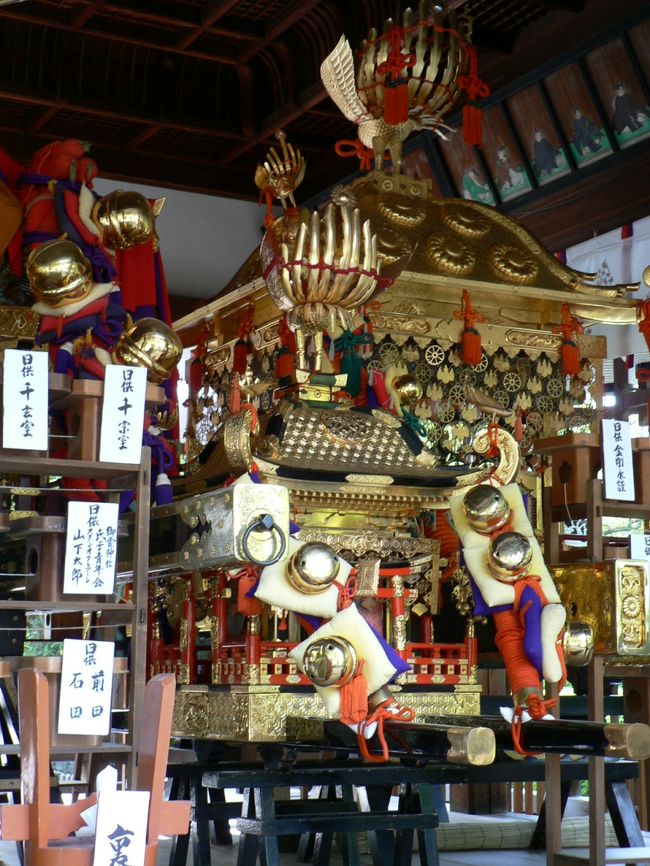 御霊神社（ごりょうじんじゃ）に近い妙覚寺（みょうかくじ）は日蓮宗の本山で１３７８年、伊豆で日蓮を救ったと言い伝えられる日実の創建とされている。 <br />室町幕府第１３代将軍足利義輝（あしかが よしてる１５３６−１５６５年）の御所となったり織田信長（おだ のぶなが１５３４−１５８２年）の上洛時の宿所となったりしており、１５８２年の本能寺の変時は嫡男・織田信忠（おだ のぶただ１５５７−１５８２年）が滞在していた。本能寺の変を知った織田信忠は二条新御所に移動しわずかな軍兵と篭城したが明智軍に攻められ自害したそうだ。 <br />御霊神社（ごりょうじんじゃ）は下御霊神社（しもごりょうじんじゃ）に対応する名前として上御霊神社（かみごりょうじんじゃ）と呼ばれるが現在は正式名を「御靈神社」としている。 <br />政争に巻き込まれて憤死した人々の怨霊を慰めるために創建された神社だ。<br />１４６７年、畠山政長（はたけやま まさなが１４４２−１４９３年）と畠山義就（はたけやま よしなり１４３７−１４９１年）との私闘・御霊合戦が境内の森でなされ、翌年勃発し１１年も争いが続き京都の町を焦土と化した応仁の乱の前哨戦となった。<br />５月１５日は５月１８日に行われる京都（洛中）で最も古い祭りと言われる例祭の御霊祭の神輿が供えられ御霊神社周辺は華やいだ雰囲気だった。<br />（写真は御霊神社の御霊祭の神輿）<br /><br />