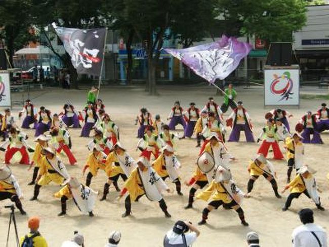 名古屋の大学生が９６年に北海道の「よさこい祭り」に参加した事をきっかけに、名古屋でも踊りで感動を与えられないかという事で、９９年の夏に「ど真ん中祭り」として、「どまつり」を立ち上げました。今では、夏の名古屋の代表的は祭りとして認識され、名古屋の夏を盛り上げる祭りとなってます。そして自分も毎年この祭りを見させてもらい夏を感じさせてもらってます。今年も例年のごとくこの夏祭りを見に行きました。８月の酷暑の中（今年は特に暑かった）、名古屋の夏の風物詩、名古屋最大の夏のいベント「第１２回　にっぽんど真ん中祭り」を栄の「ナディヤパーク矢場町公園会場」へ行きました。初めての会場そして、初めてこの祭りで使うカメラで写真がうまく撮れなくて、まして３８度を超える暑さに、今回は苦戦しました。結果満足のいく旅行記とはならなかったのですが、（とにかく暑かったので集中力がなかった）次回への勉強としました。