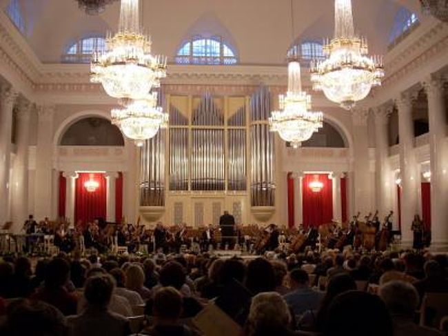 サンクトペテルブルクは音楽の聖地である。ここフィルハーモニーホール（写真１−３）では1893年コレラによる死の直前のチャイコフスキーの指揮で交響曲第6番「悲愴」が初演されている。 <br />　<br />サンクトペテルブルクフィルハーモニーはソ連時代はレニングラードフィルハーモニーと称しており、巨匠ムラヴィンスキー(1903−1984、写真５、６）を常任指揮者として、当時絶頂期にあったカラヤン・ベルリンフィル、べーム・ウィーンフィル、ショルティ・シカゴシンフォニーと並ぶ世界4大オーケストラとして君臨していた。私も学生時代にムラヴィンスキーの強烈な個性、厳格な音楽にしびれた思い出の演奏会を体験している。彼は飛行機嫌いで有名で、日本へはシベリア鉄道で演奏旅行にやってきたそうだ。また極端なレコード嫌いとしてカラヤンの対極にあるマエストロであったため、長く幻の指揮者と呼ばれていた。その後４回の日本への演奏旅行で限られた聴衆ではあるが、ファンの語り草となっており、いまだに海賊版の録音が発見されるとファンの間で話題になっている。私も彼の演奏に接して、いつか彼らの本拠地のホールを訪れたいと思っていたが、約25年を経て昨年やっと夢が実現した。 <br />　<br />彼の指揮でショスタコーヴィッチ（1906−1975）の多くの交響曲がここで初演された。最も名高いのは交響曲第5番、「革命」の名で知られるが、革命とは直接の関係がない。また1942年8月9日、ナチスドイツに包囲されたこのホールで交響曲第7番「レニングラード」は初演された。 <br />　<br />現在の首席指揮者はユーリ･テミルカーノフ（1938−、写真７）で、世界最高峰の演奏レベルを維持している。彼はロンドン、ドレスデン、ボルティモアなどにも拠点を持っている。昨年はプロコフィエフの記念の年で、私は彼の指揮でカンタータと交響曲第５番、昨年12月にはロメオとジュリエット組曲などを聞くことができた。現代の残り少ない巨匠の一人である。巨匠と呼べる指揮者の特徴は、指揮台にいるだけでオーケストラが自由自在に鳴り出す。指揮者はほとんど何もしない。円熟の巨匠だけが可能な至芸である。 <br />　<br />彼はこの年（2008年）70歳、サンクトフィル就任20周年とあわせて08年12月12日に彼のバースデーコンサートが開催された。マリス・ヤンソンス、ユーリ・バシュメット、エウゲニ−・キーシン、ギドン・クレ−メル、ナタ−リア・グートマン、ヴァディム・レーピン、庄司紗矢香などが一同に会し、ガラ・コンサートが開催され、客席にはゲルギエフの姿も見えたそうだ。これだけの顔ぶれが揃うことが度々あろうとは思えない。テミルカーノフのお気に入り、庄司紗矢香が日本人として一人参加している。（この日はサンクトペテルブルグに滞在中であったが、残念なことにこのコンサートには行けなかった。上記の情報はこのコンサートに行かれた方に直接伺ったお話である） <br /><br />この町の第２のオーケストラとして、アカデミーオーケストラがある。こちらは最近単身来日して日本でも知られるようになったアレクサンドル・ドミトリエフ（写真８）が率いている。上記のサンクトフィルと比較すると、その表現力、パワーと繊細さは開きがある（サンクトフィルが別格に優れている）というものの、この日に聴いたプロコフィエフなどお国物を演奏させると他のオーケストラにはひけをとらない。 <br /><br />サンクトペテルブルクの目抜き通りネフスキー通りの東の終点近くにあるアレクサンドル・ネフスキー大修道院（写真９）に向かう通路の両側には、18−19世紀に活躍した文化人らが眠る二つの墓地がある。ここにチャイコフスキー(写真10）、ムソルグルキー(写真11）、グリンカ（写真12）、バラキレフ（写真13）、リムスキー・コルサコフ、グリンカなどロシアを代表する偉人達の墓があり、日本を含む世界中から愛好者の訪問が絶えることがない。音楽家以外にもドストエフスキー（写真14）、カラムジン、科学者のロモノソフ、建築家のロッシ、ザハーロフ‥、ロシアの奥の深さを感じる。