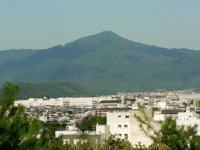 船岡山は、京都市の紫野(船岡山から大徳寺周辺一帯)にあり、標高112mの丘陵で地形が船に似ていることから古くから船岡と呼ばれていた。<br />平安京が定められる際北の基点となり、船岡山の真南に大極殿が建てられ都の中心軸として朱雀大路が造られたといわれているが、陰陽五行思想・風水思想に基づいて船岡山は大地の力が溢れでる玄武の小山であるとされたためとのこと。平安時代の初期には祭祀の場で聖地とされ山頂には祭祀の痕跡いわれている磐座(いわくら)がある。<br />平安期の王侯貴族からは散策の地として愛され、若菜摘み、わらび採りに興じる清遊の地として多くの和歌が残され清少納言も『枕草子』に「丘は船岡…」と讃えている。<br />平安時代中期以降は、一帯が葬送の地となり山腹には石仏が見られる。中世には戦略上の要所として山城が築かれ、応仁の乱の際には西軍がここを陣地にしたため、船岡山周辺一帯が「西陣」と呼ばれるようになった。<br />船岡山の南東部分には建勲神社(たけいさおじんじゃ、通称:けんくんじんじゃ)があり織田信長を主祭神とし、子の織田信忠を配祀としている。船岡山は平安京の四神相応の玄武に位置し、本能寺の変の後に豊臣秀吉が正親天皇の勅許を受け、船岡山を主君織田信長の廟所と定めていたが、明治天皇が1869年に創建し1880年に山の中腹に神社が建立された。880年に山の中腹に神社が建立されるまでは表参道にある「大平和敬神」の石碑が建っている場所に本殿があった。祭神・織田信長の業績にちなみ、国家安泰・難局突破・大願成就の神社とされ高台にある境内からは特に大文字山・比叡山方面の眺望が良い。<br />船岡山公園(ふなおかやまこうえん)は建勲神社に隣接する船岡山の西北部一帯の公園で1935年に開設している。約56000平方メートルの船岡山公園の頂上付近からの大文字山・比叡山方面,市街地の眺望は良くツツジ、ハギ等、雑木林の中に遊歩道、あずまや、藤棚などがある。<br />(写真は建勲神社から見た大文字山・比叡山方面)<br />