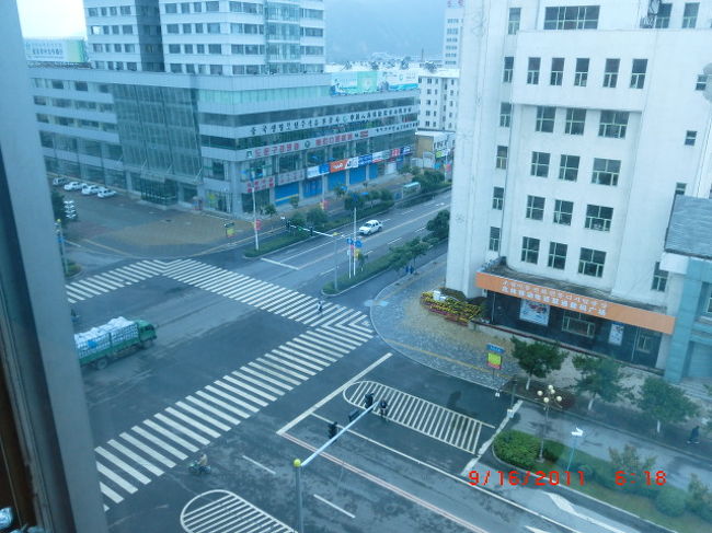 2011年9月16日、6:18:20 <br /><br />図們大厦の窓ガラスは青色 <br /><br />窓越し写真はこの色になる <br /><br />南東方向を写す <br /><br />写真左向かいの建物は「図們農村合作銀行」 <br /><br />これが高層ビルなので展望が悪い <br /><br />///////////////////////////////<br /><br />６日目：９月１６日（金）：曇り <br /><br />図們にて <br /><br />----------------------------------------<br />２０１１／平成２３年９月１６日（金）<br /><br />■図們の朝<br /><br /><br />いつものように５時頃に起床する、といっても日本時間は６時なのでその感覚のままと言う感じだが。７時半頃にホテルの朝食を食べる。 <br /><br /><br /><br />