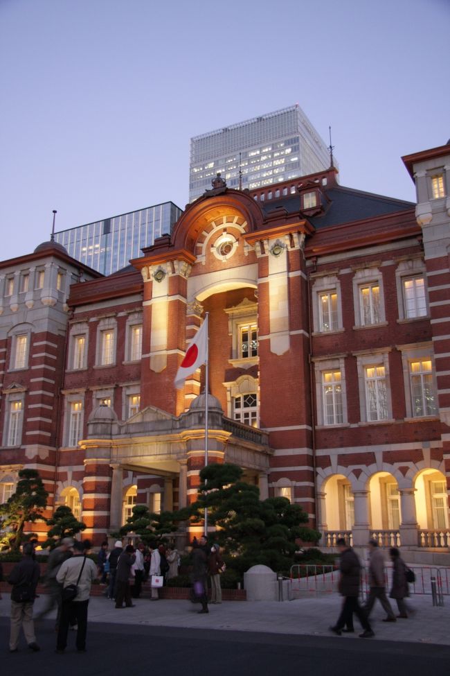 ライトアップされた復原東京駅　2012.11.27　　　16：44<br />Tokyo Station in the evening lighting<br /><br />来春のフランスグループ旅行のための渋谷JTBでの3回目の打ち合わせを午前中に済ませたあと、都内の紅葉めぐりと大改装を終えた東京駅見学の小さな旅に出かけました。<br /><br />最初の「渋谷・代々木公園」http://4travel.jp/traveler/810766/album/10730215と2ケ所目の「虎ノ門・霞ヶ関」http://4travel.jp/traveler/810766/album/10730620/」に次いで、最後は東京駅です。<br /><br />今年になって東京駅周辺の街歩き旅行記は2編公開しましたが、今回は東京駅が綺麗になっての総仕上げです。<br />http://4travel.jp/traveler/810766/album/10683181/　6月<br />http://4travel.jp/traveler/810766/album/10703899/　9月<br /><br />虎ノ門から地下鉄銀座線と丸の内線を乗り継いで東京駅へ着き、JRの案内所で東京駅ドームの場所を尋ねた。<br />地下通路のエレベータで上がると、目の前の東京駅丸の内北口の改札の外がドーム広場になっていた。<br />テレビや新聞などで何度も見たドーム内部のすばらしい美しさに「ワー　すごい」と声を出してしまった。<br /><br />ドームの上部は白・クリーム色・茶色の三色の上品な色の組み合わせで、窓から差し込む陽の光と淡い照明が100年前の創建当時の美しさを想像させてくれる。<br />ドームへ来た人の大半がカメラやスマホ、携帯などで写真を撮っていた。<br />ひととおり撮影してからは駅舎の外観を見るために丸の内側駅前広場へ向かった。広場と言ってもたくさんのガードレールが車道、歩道、小広場などに細かく区切っている。<br />三脚にカメラを据えて待っている人にライトアップの開始時刻を尋ねると4時半頃だろうとのことで、しばし休憩。<br /><br />駅舎はこの時点では丸ビルなどの高層ビルの影でほとんど陰っていたが、1箇所だけ日が射し屋根の本来の色を見せてくれていた。<br />レンガと同じ色の屋根枠と黒い天然スレートの屋根が重厚さを見せる。<br /><br />4時半になって外観の照明が始まったが、控えめにビルトインされた照明器具のために上品で落ち着いた雰囲気を醸している。<br /><br />駅前にはたくさんの人々が集まり、通り、口々にこの美しさに感嘆の言葉を発していた。<br />記念撮影する人々も満足感に満ち「はい　チーズ」は要らない。<br /><br />今回の改装に合わせてリニューアルされた東京駅ステーションホテルに行ってみたが、ロビーは見学する人で混雑していた。<br /><br />日没とともに周囲のビルのあかりと暮れなずむ空の残照が、何とも言えぬ神々しいほどの融合を見せ、好きな都会の美しさがイチョウの黄葉に劣らず私の心を高揚させてくれた（暮れた）。<br /><br />撮影　CANON EOS40D EF-S 17/85,EF-S 55/250<br />P-mode, ISO 800, WB auto<br />CANON PowerShot A2300<br /><br />参考サイト<br />http://takuya870625.blog43.fc2.com/blog-entry-1200.html<br />http://sappukei.livedoor.biz/archives/5936937.html<br />http://4travel.jp/traveler/810766/album/10710043/<br /><br />&lt;a href=&quot;http://blog.with2.net/link.php?1581210&quot;&gt;人気ブログランキングへ&lt;/a&gt;<br />