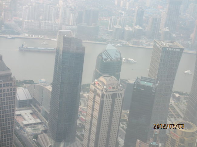 三菱製の高速エレベーターで、１分も掛らずに展望台のある９４階、４５０ｍのラウンジに運ばれる。この上海ヒルズは現在中国一の高さのビルで、六本木ヒルズと同じ所有の森ビルが作ったものだから、同じ名前の「ヒルズ」を使っているが、高さはこちらの方が遥かに高い。正式な名称は「上海環球金融中心」と言って、上海、中国のみならず、世界経済を動かす巨大なセンターとなっている。<br /><br />このビルの展望台の最上階は１０１階、４７２ｍあり、台北の１０１ビルより高く、一時は世界一高い展望ラウンジであったが、我々ツアーは入場料金の関係で、それより低い９４階止まりとなったもの。それでも４５０ｍと言ったらちょっとした小山で、当方が良く山歩きしている八王子城址公園よりも高く、ここからの見晴らしは、周囲のビルは全て下に見える。しかし今日は残念ながら空気中の湿気が多く、日本の冬空のように澄み渡った風景を眺めることは出来ず、僅かに眼下の黄埔江、その先の旧市街地、又、川を下った少し先が見える程度へ、残念ながら太平洋は靄の中に霞んでいた。<br /><br />ラウンジには土産物ショップなどもあり、このビルの特徴、てっぺんに穴が開いた栓抜き状の形をしているが、それをイメージした栓抜きなども売られているが、１個、２５０元、約４０００円もするんじゃ、余りかう人もいなかった。更にこのフロアーの売りは、ガラス張りのトイレで、４５０ｍの高さからガラスを通して放尿することであり、多くの観光客が悦に入っていた。<br /><br />先月個人旅行で来た時は、目の前の上海タワーに上ったが、ここから見るとこのタワーも子供のような大きさで、上海バンドの高層ビル街も箱庭を見ているような小ささである。腫れあがっていたら、杭州蘇州、東シナ海の島々、等見える筈だが、今日のこの天気、３６０度の展望とは言え、足元の限られた範囲しか見ることが出来ず、それが少しばかりの残念であった。