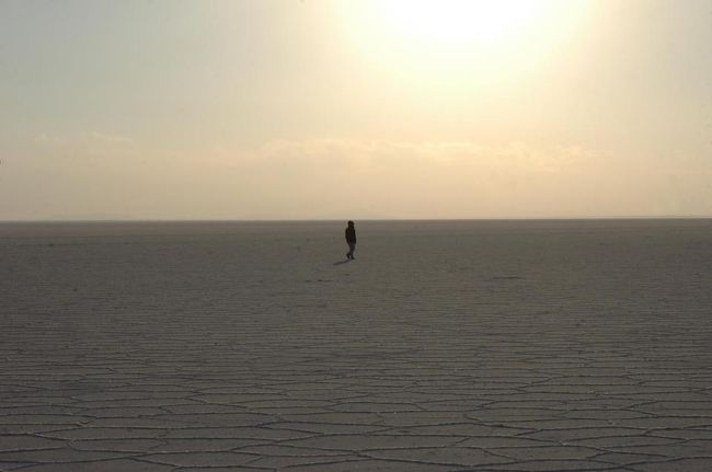 ウユニ塩湖（Salar de Uyuni）は、東西250km、南北100kmにわたる途方もない広さのフラットな塩の鏡。塩湖には島もいくつかある。対岸の見えない白い海だ。秋田県と同じ広さという人もいれば、四国の半分という人もいる。<br /><br />ウユニの街の1歩手前、コルチャニに着いた。鉄道の駅がある。どの駅もゴーストタウンのような殺風景のほこりだらけの集落だが、コルチャニもそうした駅のひとつ。7時間ほど行ったところにポトシという地理で覚えた鉱山（銀、すず）がある。鉄道は鉱山の賜物だった。<br /><br />夕日の沈むまでサラールへ車で漕ぎ出す。そう、車はサラールという海に漕ぎ出す舟だ。わだちや塩取りの小屋、ケルンだけが目印の塩の海。乾期は塩だけだが、雨期には10ｃｍくらい水に浸かる湖。車がすぐに悪くなるだろうなと思う。<br /><br />湖面が亀の子のような紋様になる。紋様は際限もなく続く。<br />湖面に降り立った時は、初めて見る自然の光景にぽろっと涙が流れた。これは何なのだろう？。「何これ？」を連発する。塩の白と空の青。夕焼けの茜色がだんだん加わってくる。亀の子を夕陽に向かって歩く者もいれば（なぜヒマワリのように太陽に向かって歩くのか？）、楽器を奏でる者もいた。私は360度ゆっくりと回ってみた。車を運転し、好き勝手な方向に進んでみた。自分が円の中心にいるような錯覚に陥る。塩を削り取ったりなめてみたり、寝っころがってみたり、逆立ちしたり、ケンケンパーしたり、それぞれが子どものように遊んだ。<br /><br />夕陽がサラールの向こうに沈むのをみんなでずっと見つめていた。沈むまで誰もそこから動かない。青春ドラマのようにくさいが、子どもになって遊んだ後はみんな素である。空の色がブルーからオレンジ、金色と変わっていく。<br />「きれい！」「すごい！」を連発。こんな時って語彙も乏しく同じ言葉を繰り返すだけ。自分が小さく見える瞬間でもある。どう形容しても伝えられない。あきらめるしかない。<br /><br />太陽が沈んでからはその余韻を楽しむ余裕はなかった。目印の殆どない、また車にGPSがついていない塩の上では、方角がわからない。彷徨う難破船になりかねない。来た方角とわずかなわだち（どの方向にも何本もある）、分岐があればどちらかに賭けて進路を取る。見覚えのある塩取り小屋を見つけたときは心の底から安堵した。温度も刻一刻と下がっていった。 <br /><br />「月の塩」というホテルは、コルチャニからわだちを通ったところにある小高い丘にある。サラールに一番近い。壁、テーブル、ベッド、棚、椅子が全て塩湖から切り出した塩の塊（塩のブロック）でできている。床は砕いた塩。きれいに掃き寄せられ、日本庭園のようだ。歩くとさくさく音がして足には柔らかい。<br /><br />雨期でも湿気で溶けないのだろうかと、湿気の多いところに住む者はつい考えてしまう。サラール中央にある、同じような塩づくりのホテルが環境問題のため閉鎖はしたもののちゃんと存在するからには大丈夫なのだろうと思う。<br /><br />サラールに向かって立つコロニアル風で、部屋の外にオープンなリビングがあり、大きく開いた窓から塩湖が見渡せる。塩平線（こんな言葉はあるのかどうか?）へ沈む夕陽の絶景ポイントだ。遠くにウユニの街、近くにコルチャニも見える。<br /><br />月の登らないLuna Salarで、星を眺めた。<br /><br />天の川が星雲に見える。南十字星には初にお目にかかった。<br />星が大きい。星がばんばん流れる。でも寒い！<br />「今からサラールの真ん中で星見よう！」という申し出には丁寧にお断りした。<br />「帰れなくなっちゃうじゃないですか、朝まで」<br />「シュラフ積んでるよ」<br />彼は本気でしたね。いくらきれいでも寒さには勝てないよ。10分見ればもう十分。<br /><br />未明には零下7度まで下がるほどの寒さなので、部屋には電気ストーブとガスストーブがたかれている。バスタブはないがお湯はちゃんと出た。私はラッキーだった。お湯か水かはこの寒さでは大問題だ。同行者の部屋はお湯が出たのは最初の3分だけだったと言って震えていた。<br /><br />そうだ、ここには檻、鉄格子、へいがない。まあ誰かが来ればわだちを辿ってくる車のほこりがそれを知らせるだろう。雨期にはたぶん鉄道でしか来られないだろう。ぐちゃぐちゃのスタックしそうなわだちを駅からタクシーで来る客もいるのだろうか？いや、タクシーは駅にはいなかった。<br /><br />2日間とも私たち一組だけのゲストだった。2日目にはカップルが来るといっていたマスターだが、来なかった。予定通り、時間通りにことが運ぶことがラッキーなこの国ではそれ自体あまり驚くことではないのだろう。TVもないし、携帯は圏外だった。<br /><br />ポトシで知事をしていたという人懐っこいマスターと関係はわからない中年女性、若い男の子、女の子の4人で切り盛りしている。マスターと女性はスペイン系に見え、男の子と女の子はアイマラの人のようだった。<br /><br />まきストーブに火が入り、ろうそくと小さな灯りでゆっくりと食事が始まる。作業をしていた男の子がボーイさんスタイルに着替えて給仕してくれる。メニューはチキンかミートと決まっている。味付けは塩、こしょうのみ。マヨネーズとケチャップはどこでも見かけなかった。日本にはいかに多くの調味料があることかと思う。デザートやジュースの種類が違うだけで2日とも全く同じメニュー。スープは、「クノールだね」とドライバー氏が指摘する。食事に出たフライドポテト。食卓塩はおいてあるが精製塩。「こちらの方が断然おいしい」と、テーブルの裏をごしごしこすってポテトにかける。 <br /><br />ボリビア記①ラパスへ<br />ボリビア記②ケーナ・サンポーニャ工房<br />ボリビア記③アルティプラノ<br />ボリビア記④ウユニ★<br />ボリビア記⑤Isra De Pesca塩湖に浮かぶ島<br />ボリビア記⑥忘れられた村Museoウユニの対岸へ<br />ボリビア記⑦ブロッケオ<br />ボリビア記⑧帰途～ハリケーンせまる