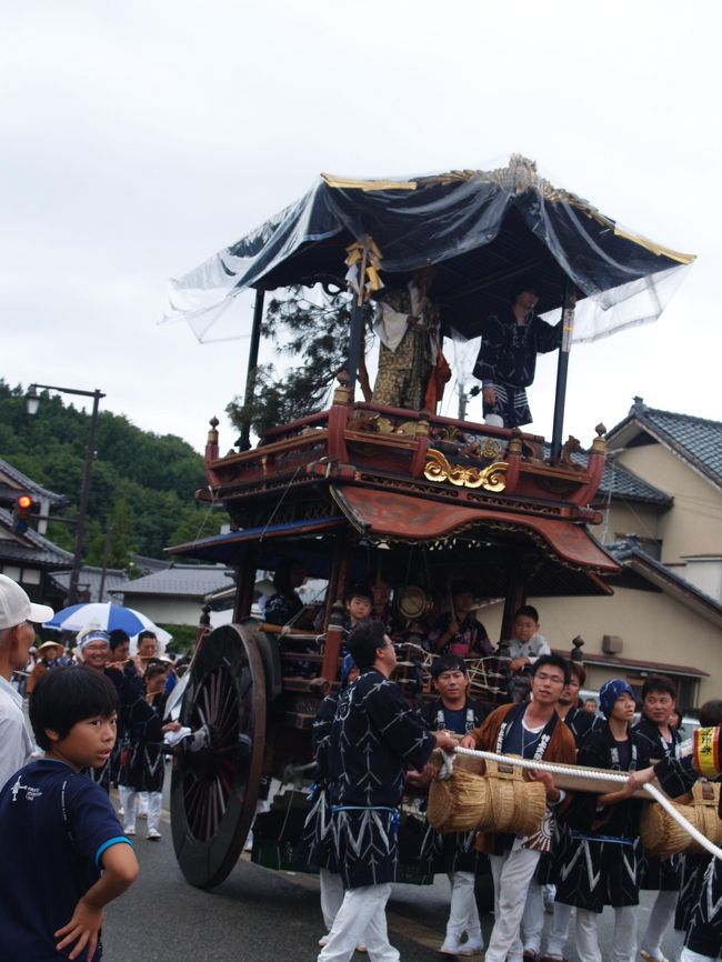 　神輿渡御の行列に続いておしゃぎり巡行が始まった。先頭1番の久保多町、2番の大町、3番の寺町のおしゃぎりに続いて4番は大工町のおしゃぎりである。<br />　大工町のおしゃぎりは寛政8年（1796年）に板垣源八・板垣政五郎治によって製作された。乗せ物は高砂である。屋台は朱漆塗りで、軽くするため、見えないように部材の内部をさくり取る技法をこらした大工の町らしいものである。残念なことに、今日は屋根の雨除けが取られないままの巡行となってしまっている。<br />　濃紺色の法被には白枠で「高砂」と右横書きされた町の印が紺色で染め抜かれている。また、おしゃぎりに乗る子供たちは浴衣姿である。<br />（表紙写真は4番大工町のおしゃぎり）