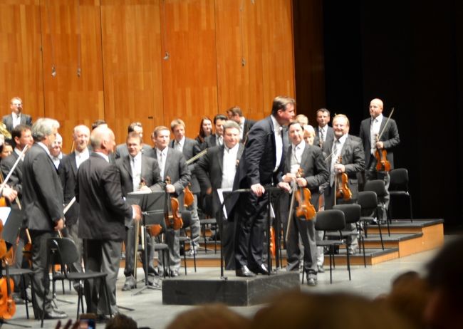 長年の念願だったザルツブルク音楽祭でクリスティアン・ティーレマン/ウィーンフィルのブルックナー交響曲第5番と、サイモン・ラットル/エル・システマ・ジュニアオーケストラのマーラー交響曲第1番他を聴くことができた。前者は祝祭大劇場、後者はフェルゼンライトシューレで、両会場の音響を比較することもできた。<br /><br />ザルツブルクと言えばモーツァルト(1756-1791)の誕生の地、1842年にすでにモーツァルト音楽祭が開催され、1887年にハンス・リヒターが参加してザルツブルク音楽祭が開始されている。そしてR・シュトラウス、ワルター、トスカニーニ、フルトヴェングラー、クナッパーツブッシュなどの巨匠が次々に参加する、世界最高レヴェルの音楽祭となる。戦後の混乱期を経て1956年、カラヤンが音楽祭芸術監督に就任、ウィーン・フィル、ベルリン・フィルを指揮、更に祝祭大劇場の建築を主導し1960年に完成、カラヤン指揮の「ばらの騎士」でこけら落しが行われた。<br /><br />小生は世界各地の主要コンサートホールでオーケストラを聴く機会を得てきたが、このフェスティバルは敷居が高かった。また、1989年カラヤンの死後、積極的にこの地を訪れる意欲が減退した、とも言える。しかし最近活躍の目覚しいティーレマンがウィーンフィルを指揮し、ブルックナー交響曲第5番を演奏する日に何とか日程調整ができそうだ。しかも翌日はラットルがエル・システマ子供達のオーケストラを指揮し、マーラー交響曲第1番を演奏する。しかもチケットはインターネットで予約でき安心して出かけることができる。これも敷居を下げてくれた大きな理由だ。<br /><br />さて、ティーレマンのブルックナーは初めて聴くが、日本でもミュンヘン、ドレスデンのシェフとして必ずブルックナーの大作を取り上げており、特に5番は難物なだけにウィーンフィルとの演奏は楽しみだ。最近の活躍ぶりは強烈な個性という点で、生粋の独墺出身としてライヴァルの、ウィーン国立歌劇場シェフのウェルザー・メストを一歩リードしている感がある。しかし彼のブルックナー第5番は正直言ってあまり期待はしていない。以前映像でベートーヴェンの演奏を見ていたが、刈り上げ君のような少々子供染みた仕草が印象に残っていた。この曲はヴァント、カラヤン、朝比奈隆の晩年の録音を愛聴しており、これを超える演奏は彼の年齢(54歳)では到底あり得ないからだ。<br /><br />ところが予想を裏切って？期待以上にいい演奏だった。連日のステージで疲れの見えるウィーンフィルも、キュッヘル、ホーネックの2人のコンマスを並べ本気の熱い演奏を聴かせてくれた。ホルンの美しい響きは常に変わりなく、オッテンザマーのクラリネットやオーボエの独特の音色は紛れもなくウィーンフィルにしかありえない。少々贅肉の付いた分厚い演奏であったが、ブルックナーの本質は外していない。彼の今後に大いに期待したい。<br /><br />一方のラットルとエル・システマである。今年のザルツブルクはヴェネズエラの音楽青少年に占領された感がある。少々長くなるが、エル・システマの理念について以下に引用しておく。<br />「1975年ホセ・アントニオ・アブレウ氏の提唱により生まれた、南米ベネズエラで現在約35万人以上の青少年が参加する音楽教育システムである。<br />政府支援のもと、子どもたちに無償で楽器と音楽指導を提供。子どもたちは、高い演奏技術だけではなく、集団での音楽体験を通じて優れた社会性（忍耐力・協調性・自己表現力）を身につけられるとして、その効果は世界中で注目されている。犯罪や非行への抑止力としても役割を果たし1990年以降は貧困と青少年の犯罪が深刻な問題であるベネズエラで、健全な市民を育成する社会政策の一環として推進されるようになり、障害者が参加するプログラムや、刑務所内における更生プログラムとしての実施も行われている。」<br /> <br />この日聴いたのは青少年オーケストラではなく、子供達のジュニアオーケストラ、ベルリンフィルのシェフとして音楽界の頂点に立つラットルが指揮を取るとあってフェルゼンライトシューレは異様な雰囲気に包まれていた。しかし何と言っても子供である。友達や保護者とはしゃいでおり、会場のいたるところでスペイン語の歓声が聞こえた。プログラムの前半は若いヴェネズエラの指揮者が登場、後半のマーラー1番にラットルは登場した。彼は子供達を相手に、時々緊張が緩みそうになるところでも一切の妥協を許さず振り切った。少々のミスはあったとしても、十分に感動的な立派な演奏で、演奏後の総立ちのスタンディングオベーションも極めて自然な反応だったと思う。<br /><br />エル・システマがこれほど全世界で評価され、展開されていることに日本人として羨望を禁じ得ない。貧困と犯罪に喘ぐヴェネズエラの青少年達のオーケストラあるから、これほど全世界的にマスコミがこぞって称賛しているが、はたして日本の高い演奏能力を身につけた子供達もこのような機会を与えられた時、ラットルの高い要求にどこまでついていけるのか、すでにハングリー精神を失ってしまっているのか気になるところだ。<br /><br />書きたいことが多すぎてキリがないのでこれ位にしておくが、ザルツブルク音楽祭を次に訪れる機会はいつ来るのだろうか。