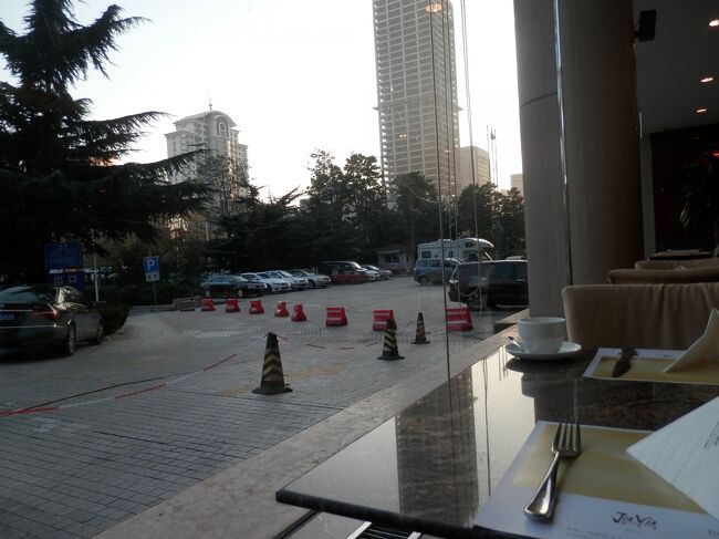 2木曜1あさ青島国敦大酒店にてホテル朝食3回<br />写真は141003-0625.朝食会場のこの薄いガラス1枚の向こうはロビーを出た人の通り道。正面がカルフル。その後ろにホテル・ホリディイン。<br />料理のケースはたくさん並ぶ。皿に取ろうと思えるのは少ない。豆乳が無くて冷たいのと熱い牛乳はある。麺のスープはしょう油の色が濃いが。味はしょっぱくない。<br />1階には、フロント、朝食会場兼レストラン、バー・セントラルがあります。