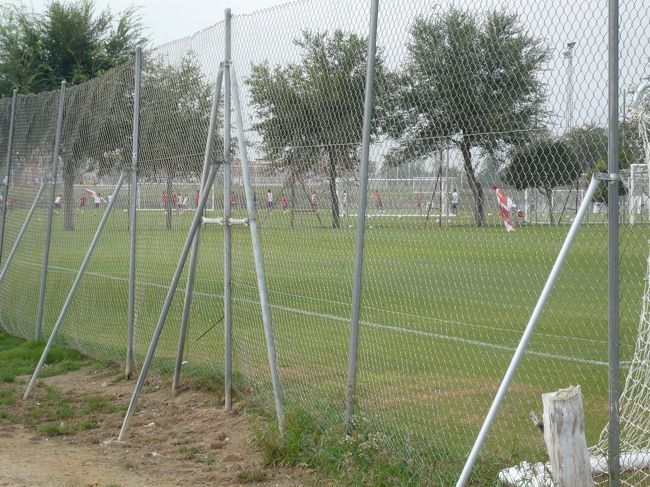 10時を迎え、Sevilla FCの練習場｢Ciudad Deportiva Sevilla F.C.｣へ地下鉄で向かう。所要20分で到着。<br /><br />施設自体は新しくは無いが、天然芝6面、Sevilla Atletico(SevillaFCの2軍。3部リーグ所属。現新潟の指宿がスペインで所属していたクラブ)用のスタジアムもあり、広大かつ充実した施設。<br /><br />カフェが併設されているので、コーヒーを飲みながら遠く行われている非公開練習を見学。しかし、ファンが殆どいない(笑)<br /><br />練習が終わったところを見計らい、トレーニングウェアで引き上げる選手に声を掛け、ユニフォームにサインを貰う。その際、｢有名選手のサインを貰いたいなら、スタジアムの反対側の入り口になるから、そっちに行くといいよ｣と教えてくれた。どうやら、Sevilla Atletico所属の若手選手だったらしい。<br /><br />急いで反対側の入り口に向かったところ、丁度高級車が一台出てきたところ。急いで駆け寄ったが、手を振りながら笑顔で行ってしまった。それが一番会いたかったバッカで会ったことに気づき、ややがっかり。<br /><br />その後3選手からサインを貰う事ができたが、以降30分待てど暮らせど選手が出てくる気配がない。<br /><br />そうこうしているうちに、地元の若者サポが｢今日は2部練習だから、けが人以外の選手はこの時間じゃ出てこないよ｣と親切にも教えてくれた。まだまだ物足らないのだが、時間ももったいないのでいったん旧市街へ戻ることにした。