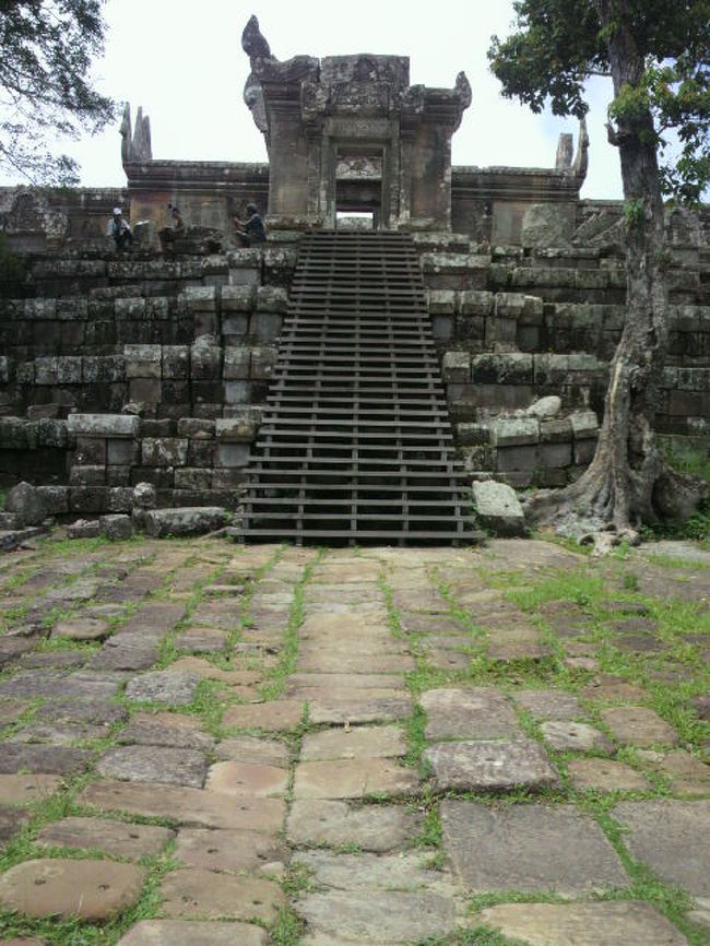 プレアヴィヒア寺院は、タイとカンボジアを分かつダンレック山脈の分水嶺に位置しており、南に広大なカンボジアの平原を眼下に収めています。<br />寺院は、山頂の南端から北側のタイ方向に、参道と階段が、なだらかに続く等斉斜面に設けられています。北端には、寺院入口の門が設けられています。<br />タイとカンボジアの紛争が激化する以前は、これら寺院地域に入るには、なだらかでかつ広い道路が備わった北側のタイ領から入るのが容易であり、ほとんどの訪問者がこの北側経路を利用していました。タイとカンボジアの関係が悪化し、国境が封鎖されると、カンボジア側から標高差約５００ｍの急峻な山道を昇る必要が出てきました。途中までは、舗装された広い道路が延びていますが、途中から急斜面の山道となっています。<br />このため麓で、入山手続きを終えた後、４輪駆動車か山道用に改造されたバイクに乗り換える必要があります。<br />山道は、寺院地域の中間部付近に続いているので、南側に、山門〜参道〜神殿等に進むか北側に下がって、入口の門から参道を昇るかいずれかを選ぶこととなります。<br />寺院の入口の先は、国境線となっていて、現在は、封鎖されています。<br />南側の突端付近に神殿があり、その先の最高点からの眺望は、素晴らしいものがあります。<br />北側には、国境線を間にしてタイとカンボジアの要員が対峙しており、立ち入りが制限されています。また道を外れると、地雷や不発弾の残る危険地域もあり、警察官等が注意を喚起しています。<br />表紙の写真は、参道から見た神殿の様子を下から見た光景となっています。