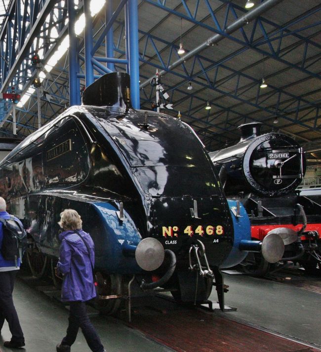 国立鉄道博物館　　2014.10.16<br />National railway Museum.York　<br />世界で初めて時速200Ｋｍを超えた蒸気機関車マラード号<br />The fastest steam locomotive in the world,Mallard.<br /><br />スコットランド・フランスの旅2014<br />写真旅行記　Travel Photo Essay<br />2014.10.13(月）〜10.27（月）15日間<br />スコットランド・フランスの旅2014<br />　<br />第7回　エジンバラからヨークへ列車の旅と国立鉄道博物館<br />From Edinburgh to York &amp; National Railway Museum<br /><br />10月16日（木）小雨（エジンバラ）のち晴れ（ヨーク）<br />ヨークへ向かう朝は4時過ぎに目覚め、しばらくして起床した。<br />荷造りを済ませ、備え付けの電気ポットで湯を沸かし、紅茶を入れてプチ（菓子）を食べて軽い朝食とした。<br />出発するまでに時間があったので、昨日観光案内所で買った絵はがきを4枚書いて切手も貼った。<br />薄暗いフロントは誰もいないのでカード・キーをカウンターに置くだけだ。支払いはチェックイン時に済んでおり、朝食もその都度精算したのでチェックアウトの手続きは何もない。できればスコティッシュ・ショーの予約などいろいろと世話になったフロントのお姉さんたちに一言礼を言いたかった。<br /><br />6時半すこし前に出かけたが、雨の後で路面がぬれていた。<br />6：40ごろ駅に着いて7：00発の列車のホームをボード（電光掲示板）で確認すると2番線で、この駅止まりの線路ではなく、通過するものだ。<br />終点の線路のホームに入るには改札ゲートがあるので駅員に確認しないと間違う恐れがある。<br />eチケットの号車を見ずに、入ってきた列車に適当に乗り込んだら、運よくチケットに書かれたＤ号車で、かなり空いていた。<br />定刻7時に発車して間もなく検札が来て、座席番号がちがうので次の駅までに指定された席に着くように注意してくれた。<br />朝の通勤・通学時間帯になるとほぼ満席になり、あらかじめ（7/31)オンライン手配しておいてよかった。<br />ちなみに通常料金の1/4ほどで買った。イギリスのて鉄道の切符は3か月前の発売日よりも、その1か月後が圧倒的に安いことを今回体験した。<br />参考：http://4travel.jp/travelogue/10935919<br />運行記録<br />Edinburgh　Waverley7:00→ Berwickon Tweed7:50→Alnmouth for alnwick8:05→Monpech8：19→ Newcastle8:35→Durham Castle8:49→Darlington9:10→York9:37(5分遅れ）<br /><br />今回の2800キロに及ぶ列車の旅の最初の区間（324キロ）で、列車がわずかの遅れで無事に到着してほっとした。<br />急ぐ旅ではないので、駅構内をざっと一巡りしてから外に出た。<br />駅前の赤くて丸いおなじみのポストに今朝書いた絵はがきを投函した。<br />ホテルまでは遠くなさそうだったがスーツケースが重いのでタクシーに乗った。5ポンド。<br />チェックインは3時とのことなのでスーツケースと手提げを預けた。駅まで歩くことにしたが、道を間違えて城壁に沿った道路を逆回りしてしまった。<br />私の街歩きは、ただ歩くだけではなく、見たり写真を撮りながらなので倍の時間がかかるが、20分ほどで駅に着いた。<br />旧市街を囲む城壁は道路より5ｍぐらいの高さ土塁の上に築かれた高さ5ｍほどの石積みの壁である。<br /><br />ヨーク駅構内を少し見回ってからPASTYの店でパスティ（肉入り包みパイ）とコーヒーの朝食。5.94ポンド<br /><br />あすはブロンテ姉妹の故郷を訪ねてハワースへ行くので、最寄りのKeighleyまでの往復切符を窓口で買った。事前にオンライン購入を試み時はシステムが故障中でダメだったが、オンラインと同じ20.9ポンドで買えた。<br />ローカル列車なので時間指定はなく、帰りの切符の有効期限は1か月だった。<br /><br />今日のメインは国立鉄道博物館で、駅から100ｍほど離れたところにあり、2棟に分かれている。<br />1829年のスティーブンソン※の蒸気機関車を始め、世界最速の時速200Kmを超えた蒸気機関車マラード号Mallardなど、たくさんの機関車・客車が展示され、子供連れでにぎわっていた。機関車が所狭しと並んでいる様は鉄道好きには堪らない魅力だが、シニアの一人観覧者は多少場違いな感じがしないわけでもなかった。<br />日本の初期の新幹線もあるが、シンプルな顔つきはここでは魅力に乏しい。<br />別棟には食堂車やサロン・カーが展示され、ホームの一つには料理の売店が並んでいた。ここでランチすればよかったと思ったが後の祭り。<br /><br />※ジョージ・スチーブンソン（George Stephenson、1781年6月9日 - 1848年8月12日）はイングランドの土木技術者、機械技術者。蒸気機関車を使った公共鉄道の実用化に成功した。<br /><br />12時半に鉄道博物館前から出るミニ・トレインに乗って市の中心部のヨーク大聖堂York Minsterまで行った。2ポンド。<br /><br />旅行記に記載のポンド／円レートは180円としたが、外貨購入の189円とクレジットカード精算の172円の中間値。<br /><br />■旅行計画要約（毎回掲載します）　<br />Abstract of the trip to Scotland and France<br />http://4travel.jp/travelogue/10935919<br /><br />イギリスは自動車会社Ｈの研究所勤務時に、1980年代初頭から90年代半ばまでローバーとの共同開発を含むjoint project(business)の機会に何度となく出張し、イギリス人から生きた英語を学んできたので、私にとっては学生時代に交流があったフランスとならび特別な親近感を抱く外国。<br /><br />しかしいつしか高齢となり、いつまで海外旅行ができるか分らなくなったため、一度も行ったことのないイングランドと地続きのスコットランドへ行ってみたくなり、半年ほど前に今年の旅行先に決めた。<br />先日のスコットランドの独立の是非を問う国民投票が公示される以前のことだ。<br />体質の関係で日本酒は全くダメだが、ウィスキーは好きで、最近は飲む機会が少ないが、昔はオールドパーのボトルキープができた古き良き時代もあった。水で割ってはせっかくの香りが薄まるのでロックがよい。<br />イギリスへ出張を繰り返していた80年代に、イギリス人に緑の三角形の瓶で知られたシングルモルト・ウィスキーの草分けグレンフィディックGlenfiddich（現在はサントリーが輸入・販売）を土産に奨められたこともあった。<br /><br />スコットランドからの帰りにヨークおよびハワースへ立ち寄るのも大きな目的。<br />ヨークは鉄道好きには聖地のような国立鉄道博物館がヨーク駅に隣接している。世界で初めて時速200Kmを超えた蒸気機関車マラード号を始め機関車103両、客車176両、日本の新幹線もあるそうだ。（ブルーガイド・イギリスによる）<br />ヨーク大聖堂や2000年の歴史を刻む城壁や城門も楽しみだ。<br /><br />「嵐が丘」を書いたエミリー、「ジェーン・エア」のシャーロッテ、「アグネス・グレイ」のアン（あまり知られていない）の3姉妹の生まれ育った荒野の中の小さな村で、シェークスピアが生まれたストラットフォード・アポン・エイボンと並ぶ「英国文学の聖地」ハワースは死ぬ前に訪れなくてはならない場所と思っていた。<br /><br />後半のフランス訪問については、<br />今年4月に1964年の東京オリンピックの直前の8月に日仏学生交流プログラムで来日したフランスの学生たち（3つの大学の内の1つ）が50年ぶりに再来日することになり、2日間の都内見学の計画づくりと案内に奔走した。<br />彼らがその後鎌倉・箱根・京都・広島・奈良・大阪を回り、帰国後のメールのやり取りでスコットランド旅行の計画を伝えたところ、その帰りにぜひフランスにも足を延ばして再会したいと言われ、誘いに乗ることになった。（7月）<br />リヨン、エクサンプロヴァンス、パリの3都市だが、いずれのお宅も部屋はたくさんあるのでホテルの手配は要らないと言ってくれているので助かる。<br />4月の受け入れ時にはコーディネーターを務めたので、奥様方を含め16人のメンバー全員と顔のつながりができているため、とても楽しみにしている。<br /><br />撮影　CANON EOS40D EF-S17/85<br />PowerShot A2300<br /><br />スコットランド・フランスの旅2014 1.東京からエジンバラまで　　http://4travel.jp/travelogue/10948376<br />スコットランド・フランスの旅2014 2.スコットランドの自然探訪<br />　http://4travel.jp/travelogue/10949966<br />スコットランド・フランスの旅2014 3.スコッチウィスキー蒸留所ツアーhttp://4travel.jp/travelogue/10951228<br />スコットランド・フランスの旅2014 4.エジンバラの街歩き<br />http://4travel.jp/travelogue/10953587<br />スコットランド・フランスの旅2014 5.エジンバラ城<br />http://4travel.jp/travelogue/10958956<br />スコットランド・フランスの旅2014　6.ロイヤル・マイルとスコティッシュ・ダンス　<br />http://4travel.jp/travelogue/10959995<br /><br />お気に入りブログ投票（クリック）お願い<br />http://blog.with2.net/link.php?1581210<br /><br />公開2015年1月11日11時11分11秒<br /><br />類似参考旅行記<br />http://4travel.jp/travelogue/10538269　4nobuさん<br />