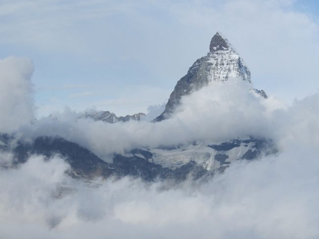 スイス観光3日目は今回旅行の、メイン観光である。<br />前日マッターホルンの街ツエルマットに到着し、町中からマッターホルンの姿が見えるかと思い、日が暮れるまでじっと眺めたが、マッターホルンにかかった雲は消えなかった。<br /> 当日朝になっても天候は回復しない。合流する予定の日本人女性ガイドに当日の天候を調べてもらい、その結果では次第に回復に向かうとのことであった。日本人ガイドは学生時代からアルプスに魅せられ、登山するうちにスイス人登山家と結ばれ、幼い子供が2人いるとかで、アルプス登山歴は長いらしい。<br /><br /> ツエルマット駅からゴルナーグラート鉄道登山列車に乗って、ゴルナーグラート展望台に向かった。乗車時間は35分弱。急坂を上る、アブト式電車で、ギリギリ歯車を噛む音が聞こえる。<br /><br /> 余談であるが、信州育ちの私はこのアブト式軌道が懐かしい。かつての信越線は群馬県の横川から軽井沢まで碓氷峠を26個のトンネルで結ばれていた。このトンネルは線路の真ん中にギアーのレールが敷設され、機関車2両増設し、先頭2両と最後尾1両の3両の蒸気機関車で運行されていた時代があった。信越線が電化され、バイパスが新設するまでの話であるが。<br /> 乗車したことはないが、箱根で運行されている電車は部分的にこの方式であると聞いたがどうだろうか。<br /><br /> ゴルナーグラート駅に到着するとそこはゴルナーグラート展望台である。標高は3089m。展望台にはホテル、記念館、その他施設が存在するが、360度アルプスの山々を見渡すことができる。<br /> お目当ては右にマッターホルン(4478m),左にアルプス第2の高峰モンテローザ(4634m)、その間にLiskam(4527m),Castor(4228m),Polluk(4092m),Breithorn(4164m)などの山脈(やまなみ)であろう。<br /> しかしツエルマットのホテルを出る頃は山脈(やまなみ)は雲の中であったが、展望台に到着したころのマッターホルンはまだ雲海から峰が顔を出し始めた頃であった。次第にマッターホルンの姿が現れ始め、すべてが現れることはなかったが、その姿には満足でき堪能した。<br /> アルプスには3大北壁と呼ばれる名峰がある。その1つはマッターホルンであることは間違いないが、マッターホルンには北壁と東壁があるという。 写真で見るかぎりでは右側の壁かと思うが、何かの機会に確認することにする。ちなみに3大北壁とは、明日観光予定のグランドジョラスと翌々日観光するアイガーである。<br /><br /> 展望台には1時間ほど周囲のアルプスの山脈を眺め観賞し、登山列車の駅に向かった。途中リッフェルアルプ駅で下車し、「カラマツ香るグルン湖往復コース」第一のハイキングである。<br /> 歩行距離は往復5kmぐらいであるが、最高地点との高低差は89mある。<br />最初は初級コースで、抵抗感はなかったが、歩き始め最高地点近くまで歩いたが、道はガレ場の坂道で、かなり消耗してしまい、今後の旅行日程に支障をきたす恐れを感じ、残念ながら山小屋がある地点で、リタイアし、本隊が戻るまで休憩した。再びリッフェルアルプ駅から登山列車でツェルマットに戻り、この日の観光を終えた。<br /><br /> <br /> <br />