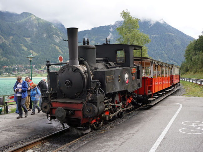 チロル州の州都インスブルックからザルツブルク/ウィーン方面にオーストリア国鉄ÖBBの列車で20分ほど、イエンバッハの駅で接続するのがアッヘン湖鉄道（アッヘンゼー鉄道/アッヘンゼーバーン）。<br /><br />標高530mのイエンバッハから970mの峠を越え、標高931mのアッヘン湖を結ぶ全長6.8km、線路幅1mの狭軌路線で、1889年の開業以来130年近くにわたって、蒸気機関車だけで運行してきました。<br /><br />アッヘン湖鉄道には1000分の160の急こう配があるため、イエンバッハを出てから途中の列車交換駅エーベンまでの間には、線路の間にリンゲンバッハ式のラックレールが設置され、これに車両の歯車を噛み合わせて登ります。<br /><br />全線の所要時間50分。終点、アッヘン湖の湖畔のゼーシュピッツでは、遊覧船に接続しています。<br /><br />ウイキペディアによると、アッヘンゼー鉄道は、1889年の開業時に1号から4号まで4両の蒸気機関車を導入したそうです。4号は第二次世界大戦後に他機への部品供給のため書類上は一旦廃車となります。それ以後2005年までは残った3両で運行してきたが、古い部品や予備の部品を使って4号機が再建され、4両体制に戻ったのだとか。<br /><br />イエンバッハからアッヘン湖を往復する、クラシックなSL列車を詳しくご紹介します。<br /><br />なお、下記のURLでは動画も掲載しています。<br />イエンバッハからアッヘン湖へ往路。<br />https://omoidenoshasoukara.web.fc2.com/tabinoshasoukara/achensee/achensee1.html<br />このページの下の方。<br />アッヘン湖からイエンバッハへの復路。<br />https://omoidenoshasoukara.web.fc2.com/tabinoshasoukara/achensee/achensee3.html<br />このページの中ほど。