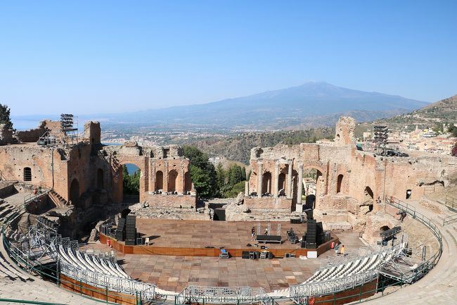 ７年ぶりのイタリア旅行。<br />前回は、東日本大震災の翌日から出かけたためバチが当たり、連日の雨。<br />しかも一番楽しみにしていた青の洞窟も波があってクローズとなり、さんざんな旅行になってしまいました。<br />そのリベンジを兼ねて、天候が最も安定する７月に出かけてきました。<br />今回の旅程は、<br />７月１０日（火）関空よりフランクフルト経由ローマに行き宿泊<br />７月１１日（水）ローマからパレルモに飛行機で移動し、パレルモ市内観光<br />７月１２日（木）世界遺産のアグリジェントとカルタジローネを観光し、タオルミーナで連泊<br />７月１３日（金）タオルミーナとシラクーサ観光<br />７月１４日（土）タオルミーナからアルベロベッロへバスで大移動し、アルベロベッロ観光<br />７月１５日（日）マテーラとポンペイ遺跡を観光しナポリで宿泊<br />７月１６日（月）カプリ島とアマルフィー観光後ナポリ泊<br />７月１７日～１８日ナポリよりフランクフルト経由関空に移動して帰宅。<br />今回は、旅物語の７泊９日のパックツアーでしたが、参加者が少なくゆったりとした旅でした。<br />天候にも恵まれ、連日の３０度越えで観光は大変でしたが、日本と違い湿度が低いので日陰に入るととてもさわやか。<br />逆に日本のほうが連日の猛暑で体調を壊しそうでした。<br />今回は、旅行３日目の午前中のタオルミーナ市内観光と夜のタオルミーナを紹介します。（午後から観光したシラクーサ観光は次の旅行記で紹介します。）<br />シチリア島のタオルミーナは、紀元前５世紀頃にギリシャ人によって開かれた都市で、シチリアの交易拠点として大いに栄えた町です。<br />今も古代から中世の歴史的建造物が残る素敵な町でした。