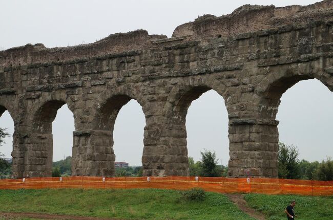 古代ローマの土木・建築技術の高度さを今に残すものの一つが水道システム及び水道橋であろう。水道橋遺跡に関しては、フランス南部のポンデュガールやスペインのセゴビアにあるものが特に有名で世界遺産にも登録されている。一方、ローマは当時100万都市であり、500年かけて建造された11本の水道から供給された水は1日に100万m3、1人当たり1m3/日と、現代の東京都民の水使用量233Lを上回る供給量であった。また、ローマ水道の精密さは有名で、通常、1kmあたり34cmの高低差で自然に流れるように設計されており、効率よく大量の水をローマ市内へ運んでいた。<br /><br />これからバスで向かうローマ水道橋公園には、6本の水道遺跡が残っており、今でも見ることが出来る。見た目には2本しか見えないが北側の背が低い方の水道橋にはユリア水道、テプラ水道、マルキア水道 、そして16世紀に改修されたフェリクス水道が、南側の背が高い方の水道橋には新アニオ水道、そしてクラウディア水道が通っていた。表紙の写真は南側の新アニオ・クラウディア水道橋だが、映画のロケにも良く使われるイメージ通りの水道橋である。<br />