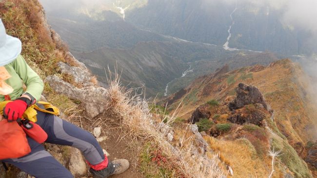 かつて「魔の山」と呼ばれた谷川岳。登山口となる上越線の土合駅前には谷川岳で犠牲となった5百余名の遭難者の名が刻まれた墓碑がある。途方もない犠牲者の数は日本一、いや世界一とも言われる。この「魔の山」も土合口からロープウェーとリフトを使って天神尾根からトマノ耳とオキノ耳の頂をめざすコースは多くの登山者が楽める安全な道である。10月9日、紅葉を楽しみながらこの天神尾根から双耳峰の2つの頂を目指した。<br /> ロープウェーの土合口駅は多くの登山者が列をなし、天神平から熊穴沢避難小屋、さらにその先の岩尾根の一帯は登山者の渋滞ができる状況だった。頂である「オキノ耳」から魔性の山を象徴する岳の東面、マチが沢や一の倉沢の紅葉を期待したが薄くガスで覆われており残念であった。