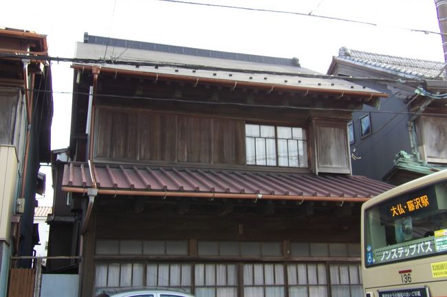 由比ガ浜通りには3棟の日本建築の建物が並んで残っている。ここは長谷寺門前に当たり、通りに面した間口が同一であるからいずれも商家であったのだろう。その最初の家は文化3年(1806年)創業の老舗商家「萬屋本店」の隣にある。「萬屋本店」はリノベーションされて3年前にレストラン・結婚式場に変わった(https://4travel.jp/travelogue/11467550)。その隣の古民家もレストラン「長谷 紫 - ゆかり -」に改装中(https://4travel.jp/travelogue/11467551)であり、開店真近になっている。次々と同じ通りの古民家がリノベーションされて別のお店に変貌して行く中で変わらない佇まいを見せてくれている。マイカーのくりくりしたヘッドランプとカエルの顔をイメージさせる特徴的なエクステリアデザインで人気だったコンパクトカー・マーチも家の前の軒先に駐車しており、変わらない光景だ。いつまでも鎌倉に残しておきたい門前町の風景だ。<br />(表紙写真は由比ガ浜通りの和風古民家)
