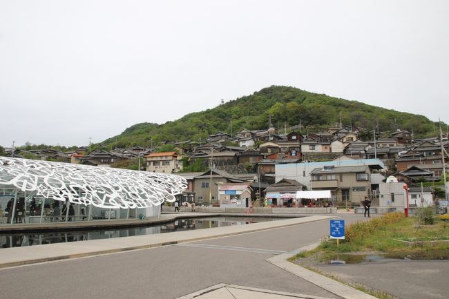 男木島、高松港正面に広がる瀬戸内海、この高松港から一番近くにある島が女木島、そしてそのすぐ北側にある小島が男木島です。男木島は、三角形を立てたような形の島で、その形状から島のほとんどが山であり、平地は港付近のごくわずかな部分しかありません。このため、この島は港から山裾を登って行くように集落が形づくられています。このように集落が山の斜面にへばり着くように形成されていることから、道もつづら折れの細い坂道がまるで迷路のように民家の間を這うように巡らされています。実は、この迷路のような道は、古来から瀬戸内を荒す海賊に対しての備えでもあった、とも言われています。男木島のお隣、鬼ケ島である女木島はかつて海賊島だったとも言われています。この対照的な性格のふたつの島が隣同士であるというのも面白いお話です。<br />そして、このように狭い坂道が多い男木島、この島の物流を支えるのがオンバと呼ばれる小さな手押し車です。この島では、港から坂の上のお家へ荷物を運ぶのに昔からオンバが使われ、今もこのオンバは島の人々にとって、なくてはならないものとなっています。<br />2013年の芸術祭では、このオンバを芸術作品とした工房が、島の古民家を利用して作られました。それがこの島の代表的なアート作品でもあるオンバ・ファクトリーです。この島を訪れると、島のおじいちゃんやおばあちゃんたちが、色鮮やかな、そして奇抜なデザインのオンバを押しておられるのを目にすることができます。現在アートが島の生活の中に完全に溶け込んでいるのがわかります。<br />現在男木島には、約170人の島民が住んでおり、過疎化によって島の高齢化も進んでいます。ただ、この男木島は奇跡の島としてある一面で大きく注目されています。なんと一旦廃校になった学校が復活したのです。これは、2013年の芸術祭を機に家族で島にUターンされたり、新たに移住されたりする方がおられ、幼児や小中学生が島民としてこの島に加わりました。これを受けて、高松市は男木島の小中学校を再建し、復活させることとなりました。その後も男木島では移住者が増加しており、今年はまた新たな移住者がなんと海外から訪れるということまで起きています。島への移住希望者に対しては、この島に家族でUターンされた方が対応する仕組み作りもなされており、小さな離島にあって人口増が実現している、まさに奇跡の島なのです。<br />瀬戸芸を通じて島を訪れた人々、こと都会で日々あわただしい生活の中に暮らす人々にとってこの島の情景を目にしたとき、自然とアート、そして島の人々の温かさなど、多くの魅力を感じるのかもしれません。人としての生活について、新たな方向性を提案してくれるというのも、この島の魅力のひとつではないでしょうか。<br />