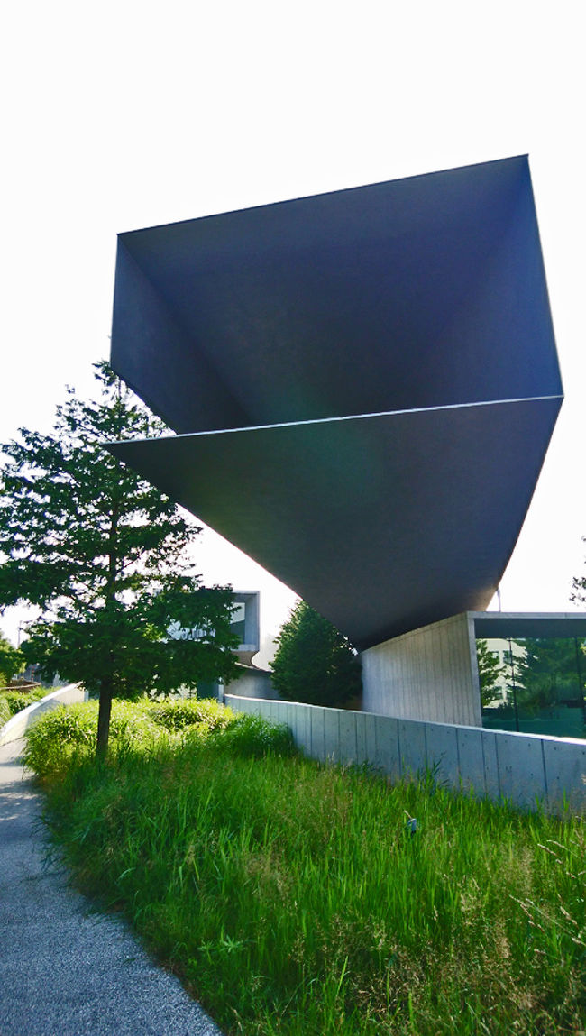 日建設計によるホキ美術館を見にいきました。内部は写真撮影禁止なので、酷暑の中、外観を撮りに覚悟して1周しました。かなりユニークな構成になっています。上空から見るとよくわかるのですが、「バランスドラーメン」という鳥居のように、内側に円弧をずらすと、中央部の構造体の重さとキャンティレバーで跳ねた部分の重さが釣り合い、柱に水平方向の力が加わらなくなることだそうです。<br />上部のチューブ状ギャラリー端部は、約30cmのキャンティレバーで張り出し周辺からのランドマークともなっているという。<br />地面レベルのチューブは、地面から約60cm浮いて設置されています。<br />地下のチューブ部分は、RC造、上部のスチール板の構造とは、部分的に接合しています。