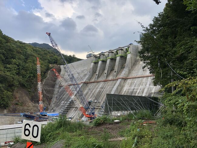 八ツ場ダムの歴史は、1947年（昭和22年）9月のカスリーン台風によって利根川流域で大洪水が発生したことに起因しています。この災害で死者・行方不明者は1,930名、これを契機として利根川の治水工事が本格化しました。<br />ところが、利根川水系の上流に位置する吾妻川流域の住民の多くはダム建設に反対し、1966年（昭和41年）1月にはこの地を地盤とする中曾根康弘衆議院議員（後に第71代内閣総理大臣）が「ダムというものは軽々しく造るものではない」と発言し、反対派を勢いづかせました。<br />その後の紆余曲折を経て1994年（平成6年）3月に建設省が付帯工事に着手したものの、2009年（平成21年）9月になって、民主党政権の前原誠司国土交通大臣は八ッ場ダム本体工事の中止を表明しました。<br />2012年（平成24年）12月に自公連立政権が復活すると、八ッ場ダム事業の推進を打ち出し、本年（2019年）9月に本体工事が完了する予定です。<br />10月からは水を貯め始め、貯水試験を経て2020年（令和2年）4月の運用を目指しています。<br />今回、異業種交流の集まりで工事現場を見学する機会を得て、関係者の様々な思いを感じた次第です。 <br />