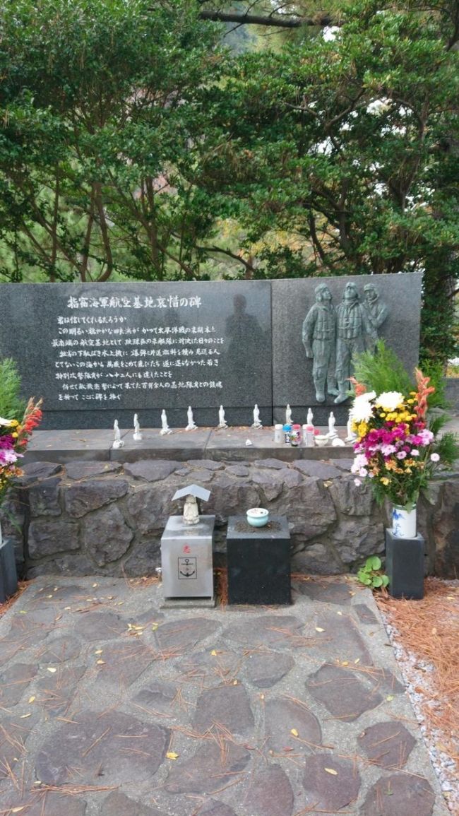 11月23日、妻と二人で鹿児島空港に降り立った。<br />今回の旅の目的はベトナムで日本の文化や習慣を教えた女性たちに合う事が一つ。<br />もう一つは指宿にある海軍航空基地跡の碑に詣でる事。<br /><br />リムジンバスで鹿児島市に入り、宿泊先のプラザホテルに荷物を預けて加治屋町の観光に出かけた。<br />ところが風向きが悪く、桜島の噴煙が降り注ぐ。<br />傘をさしている人も居るくらいである。マスクをつけたが、服が直ぐに灰に覆われてしまう。<br />維新ふるさと館を見ただけで早々にホテルに引き上げた。<br />こんなところで生活している鹿児島の人はすごいと思った。<br /><br />シャワーを浴びて気を取り直し、3年前屋久島に行くときに知り合った人がやっている居酒屋「にこいち」に出向いた。<br />天文館公園の傍に在り、安くて美味しいと評判のようだ。<br />7時位には満席になるとの事。<br />開店の5時に入店してマスターと会話を楽しみ、混み出してきた6時半には店を後にした。<br /><br />翌日24日は雨の中、レンタカーで志布志市に向かう。<br />昼前に目的地に到着して、5か月ぶりに3人のベトナム人女性に会う。<br />「うなぎ太郎」で昼食を取り、国民宿舎の日帰り温泉に向かう。<br />妻の云う事には、彼女たちは人前で裸になるのは初めてで、かなりのカルチャーショックだったようだ。<br /><br />その後雨も上がったので、都井岬へと向かい天然記念物の岬馬を見物した。<br />更に灯台50選に選ばれている都井岬灯台を見学。<br />空はどんよりしていたが、なかなかいい景色だった。<br /><br />夕方になり志布志市内に戻り、夕食に「そば茶屋吹上庵」でソバを食べて彼女たちを寮まで送り届けた。<br />別れ難かったが、妻も同じと見えて彼女たち一人一人を涙を流しながら抱きしめていた。<br />自分の子供が外国で働くことを考えたら心配で心配で、とても他人事とは思えなかったとの事。<br />100年前は日本も貧しく、ハワイや南米等に移民や出稼ぎに行っていた。<br />今は、よその地域から日本に働きに来る時代になった。<br /><br />今日の宿は日帰り温泉で入った国民宿舎ボルベリアダグリ。<br />ベットの部屋を頼んでいたので、一番端の部屋だった。<br />温泉はサウナや電気風呂もある。露天風呂は無い。<br />翌日25日は朝食を挟んで2回風呂に入った。<br /><br />9時半に宿を出発。<br />途中で隼人にあるAZと云う、家以外は何でも売っているというスーパーに寄ってお土産を買った。<br />指宿市に入り、タケトラというラーメン屋に入る。<br />ここの主人の顔が我が息子にそっくり。<br />一緒に写真を撮る。<br />海の直ぐ側にある砂風呂砂湯里という処で砂蒸し風呂に入った。<br />その後系列の「たまて箱温泉」の露天風呂に入る。<br />ここの露天風呂は海の向こうに開聞岳が見えて、とても素晴らしい景色だ。<br /><br />それから今回の本当の目的地、指宿海軍航空基地跡に向かった。<br />それは休暇村指宿の直ぐ側にある。<br />この地はかつて偵察が目的の水上飛行機の基地だった。<br />しかし沖縄戦の激化に伴い航空機不足で下駄ばきと呼ばれた水上飛行機までが特攻に使われた。<br />性能が格段に落ちる下駄ばき機での特攻はほとんど効果が無かったと思われるが、それでも飛び立たざるを得なかった不条理さにやり切れ無い思いを抱く。<br />当時10代の若き男たちはそれでも愛する家族や恋人の為に飛び立っていった。今の我々にその様な覚悟が持てるだろうか。<br /><br />知覧や鹿屋はまだしも観光案内に記載があるが、この地は一切触れられていない。<br />福岡から来たという老人が慰霊碑に熱心に何事かを語りかけていた。<br />私達はそれが終わるのを待ち、辺りを掃き清めた。<br />忘れ去られた時が本当の死だという。<br />私はこの地の出来事を伝えていくつもりだ。<br /><br />25日最後の宿泊地は「こらんの湯 錦江楼」<br />南国のリゾートムードたっぷりの処だ。<br />露天風呂は17時までは貸切に使用され、自由に入れるのはその後の時間。<br />直ぐ側を電車が走る音が聞こえる。<br /><br />26日最後の日には道の駅山川港「活お海道」でかつお節等を買い込んだ。<br />更に池田湖に向かい、往時のイッシー騒ぎを懐かしんだ。<br />その後、226号線南薩摩路を一路鹿児島市へと向かった。<br />レンタカーを返却して空港に向かい、空港の2階で鶏飯(けいはん)のバイキングで昼食とした。600円とチョー安い。<br />鶏飯は今回の旅行で気に入った料理の一つである。<br />離陸までだいぶ待ち時間が有るので、本を買ってコーヒーを飲みながら読書で時間をつぶした。<br />帰路は名古屋経由で何事も無く帰宅することができた。<br /><br /><br /><br /><br /><br /> <br /><br /> <br />