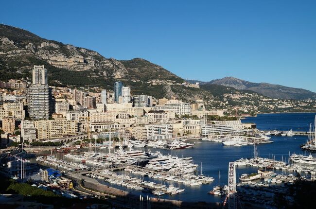 モナコ公国はフランスの地中海沿岸地方コート・ダジュールのイタリアとの国境近くに位置する世界で2番目に小さいミニ国家。国連加盟国の中では世界最小である。周囲を険しい山に囲まれ、平地は無く、上へ伸びるか(高層ビル)、下に潜るか(地下トンネル)しか無い場所に立地している。モナコはカジノで有名だが、F1モナコグランプリ、WRCラリー・モンテカルロが開催されることでも知られる。 タックス・ヘイヴン(所得税非課税)であることなどから住民の84%が外国籍(フランス国籍47%、イタリア国籍16%、その他21%)で、モナコ国籍者は16%しかいない。 <br /><br />写真は大公宮のある丘の展望台から撮影したモナコの港。お天気に恵まれたので、コート・ダジュールの群青色がより深い藍色に見えた。<br />